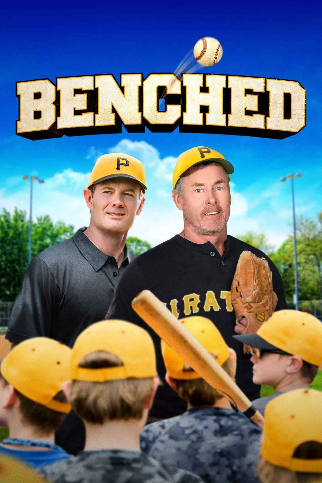 影視老將John C. McGinley自信亮相 壁紙 — 兩位戴黃色帽子的棒球教練站在年輕球員面前，在晴朗的藍天下，陽光普照的球場上，他們上方有粗體字 'BENCHED'。