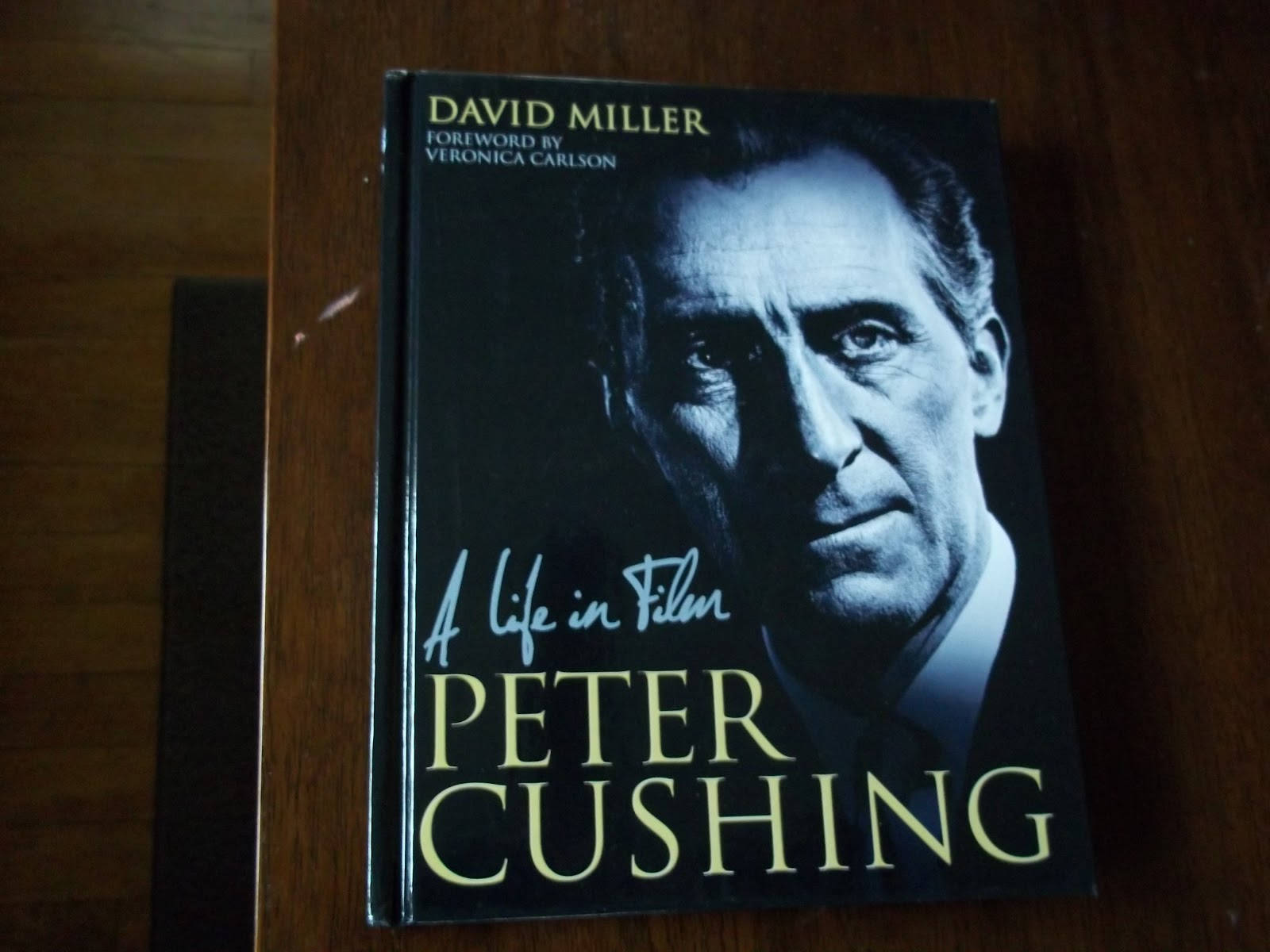 彼得·庫欣：電影人生自傳書 壁紙 — 一本名為《Peter Cushing: A Life in Film》的簽名精裝書，在溫暖的燈光下放置在木質表面上。
