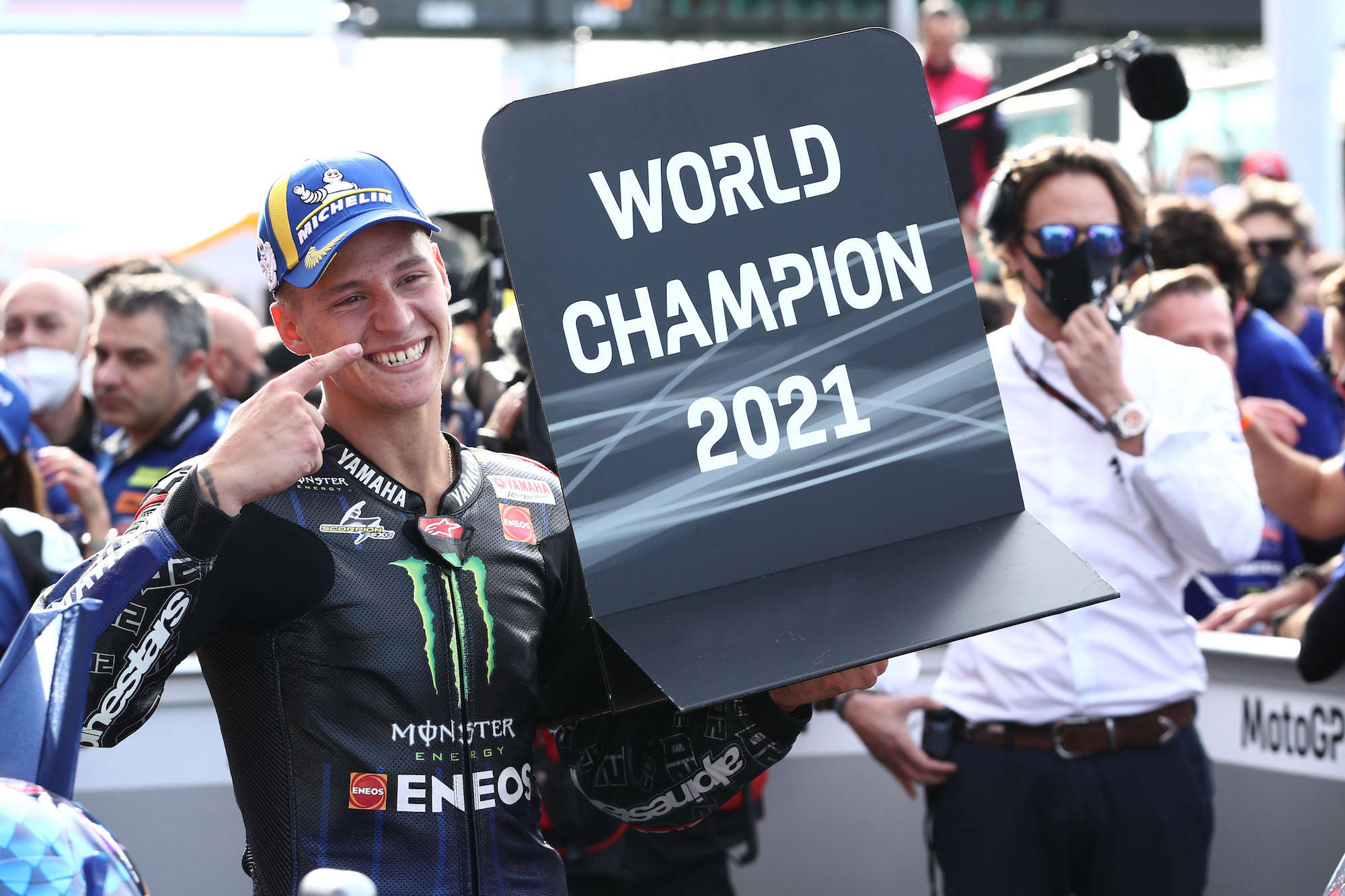 征服巔峰的冠軍 壁紙 — 一位MotoGP車手自豪地舉著「World Champion 2021」標誌，同時指著自己的臉。