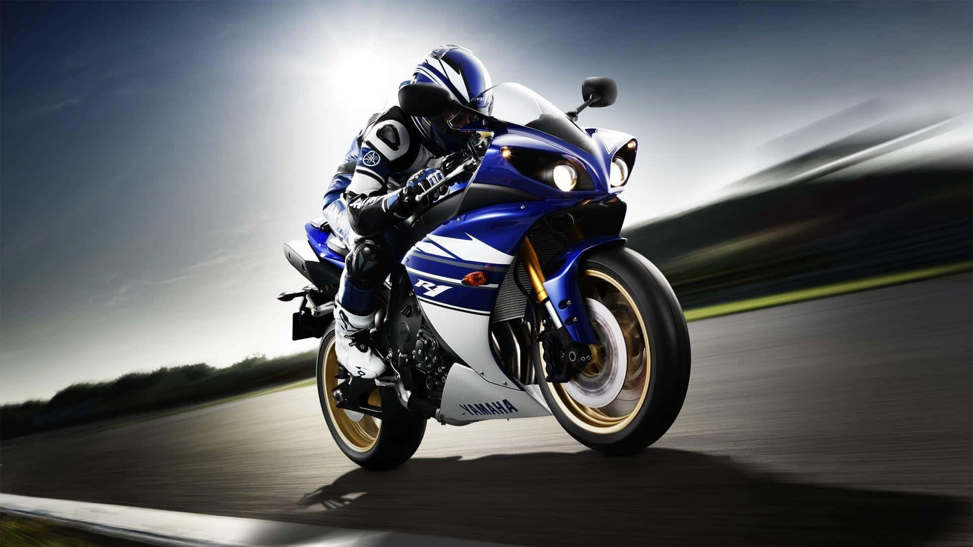 征服當下，勇敢騎手 壁紙 — 一架藍白色Yamaha R1電單車在賽道上高速行駛，帶有動態模糊效果，車手背後有明亮的陽光。