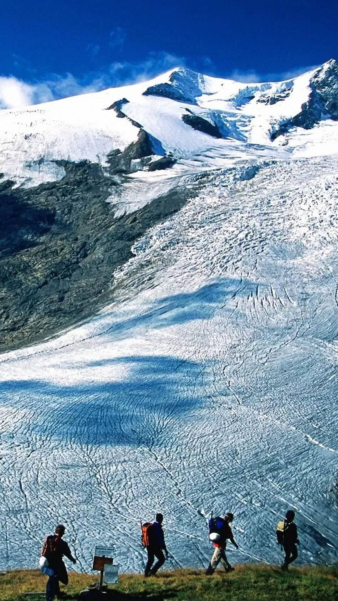 四名遠足者在積雪山脈附近的冰川上行走。