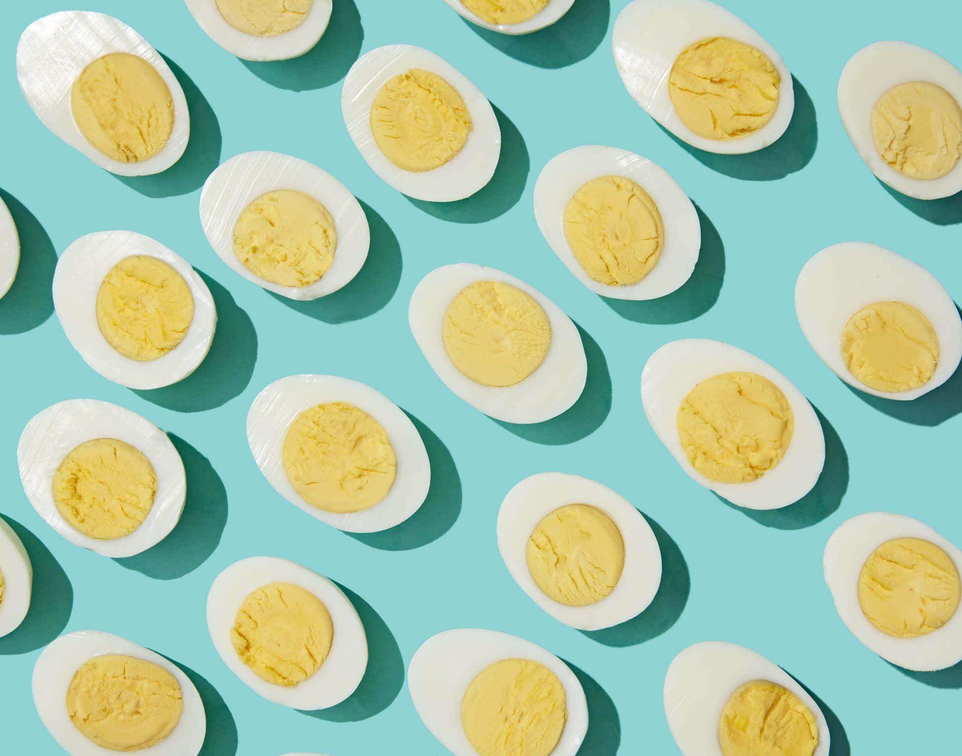Egg 桌布 壁紙 — 從上方俯瞰，半個水煮蛋整齊排列在充滿活力的藍綠色背景上，帶有柔和陰影。