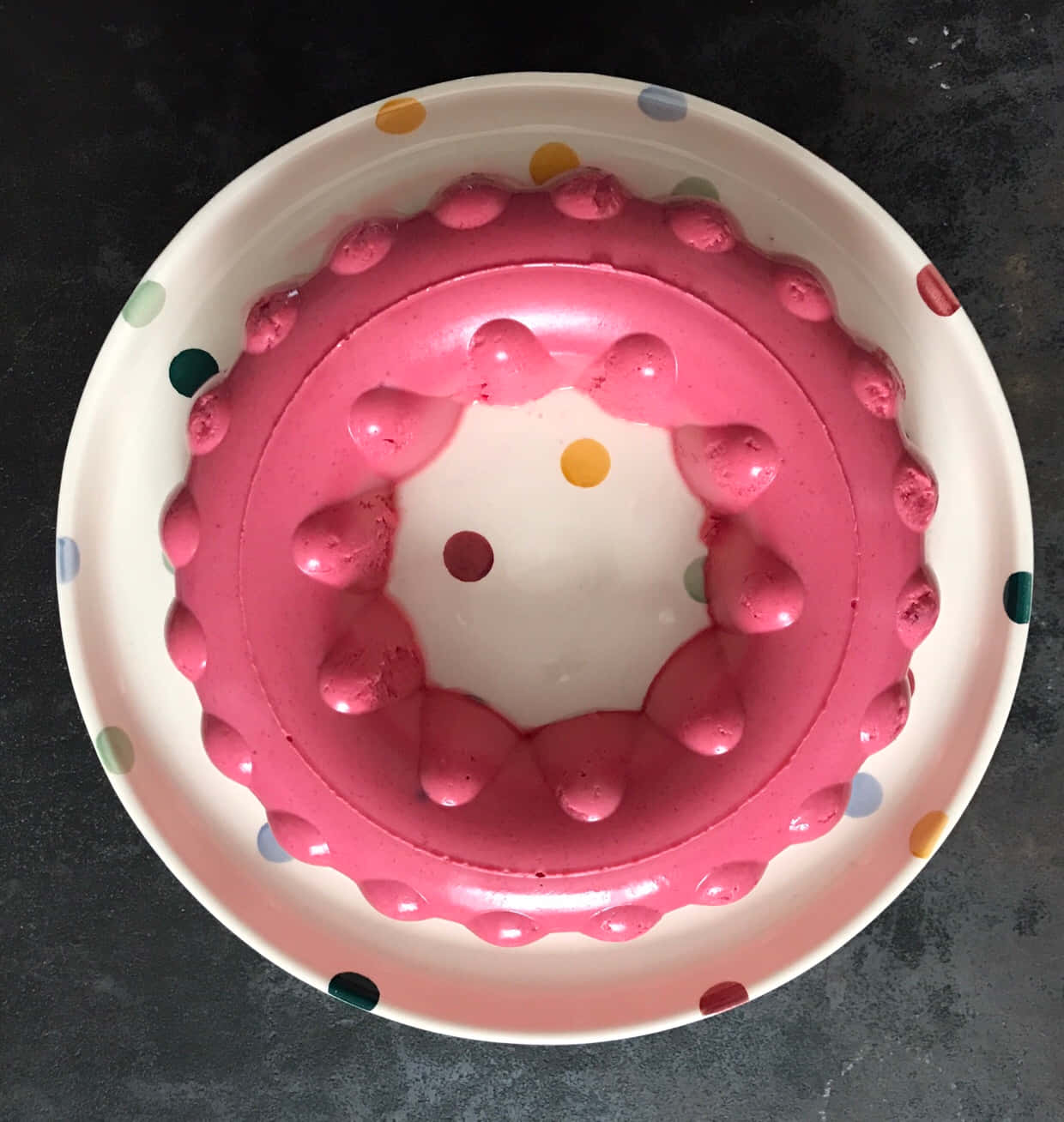 Blancmange 桌布 壁紙 — 從上方俯瞰一個深色枱面上的圓點碗中的粉紅色啫喱甜品。