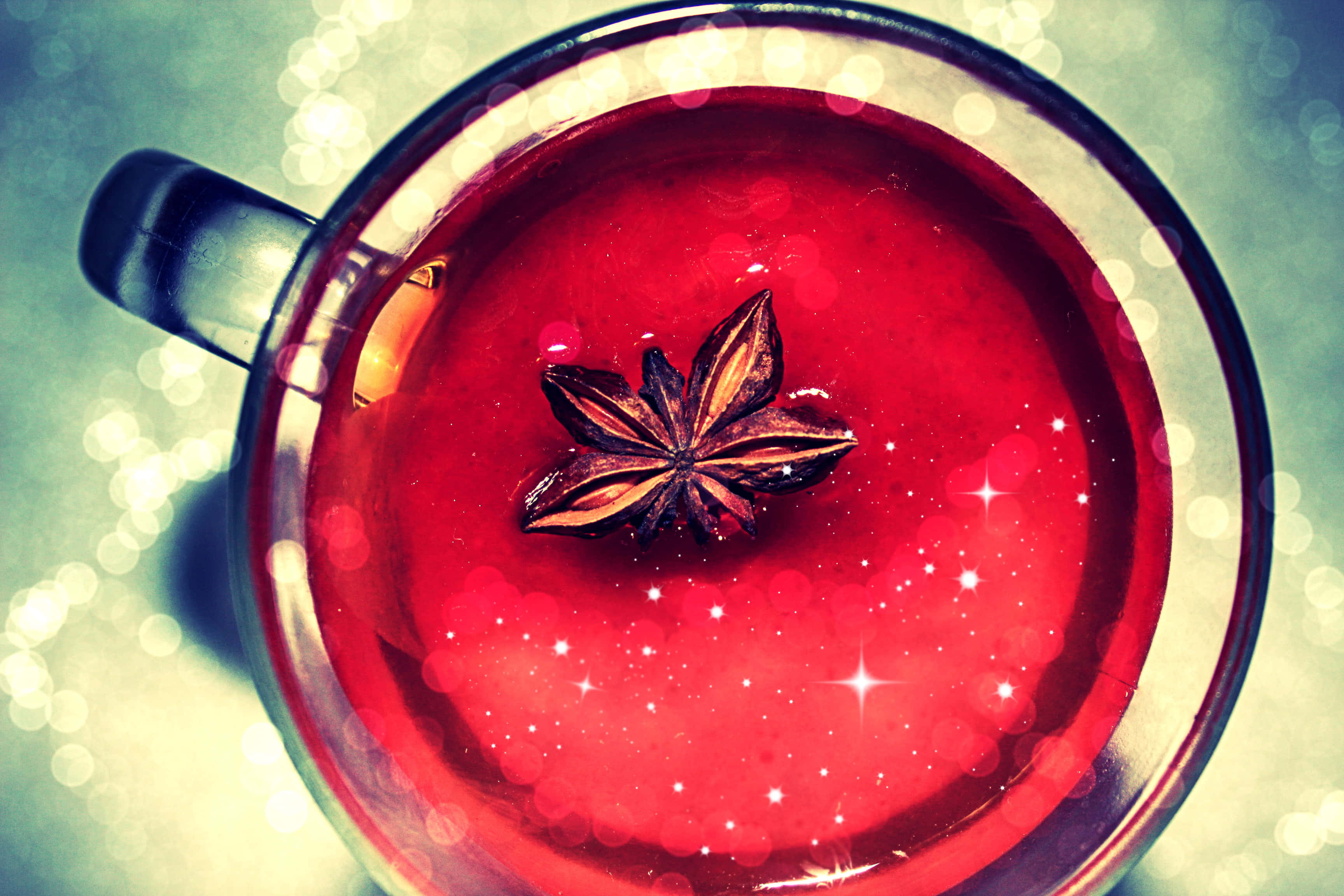 Mulled Wine 桌布 壁紙 — 從上方俯瞰一個玻璃杯，裡面裝滿了發光的紅色香料飲料，上面放著一顆八角茴香和閃爍的散景燈光。