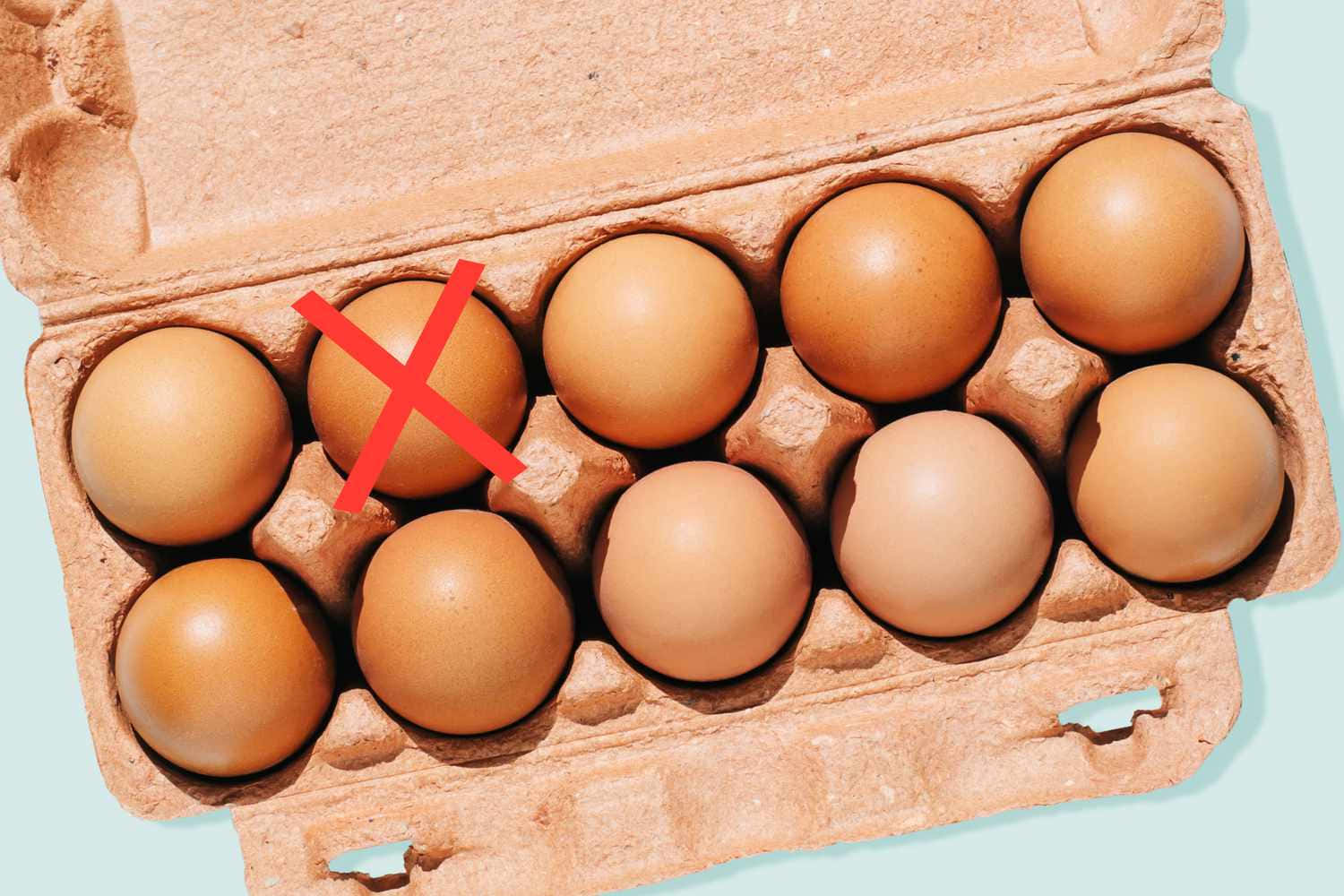 Egg 桌布 壁紙 — 從上方俯瞰一個紙板雞蛋盒，內有十隻棕色雞蛋，其中一隻標有紅色X記號，背景為淺藍色。