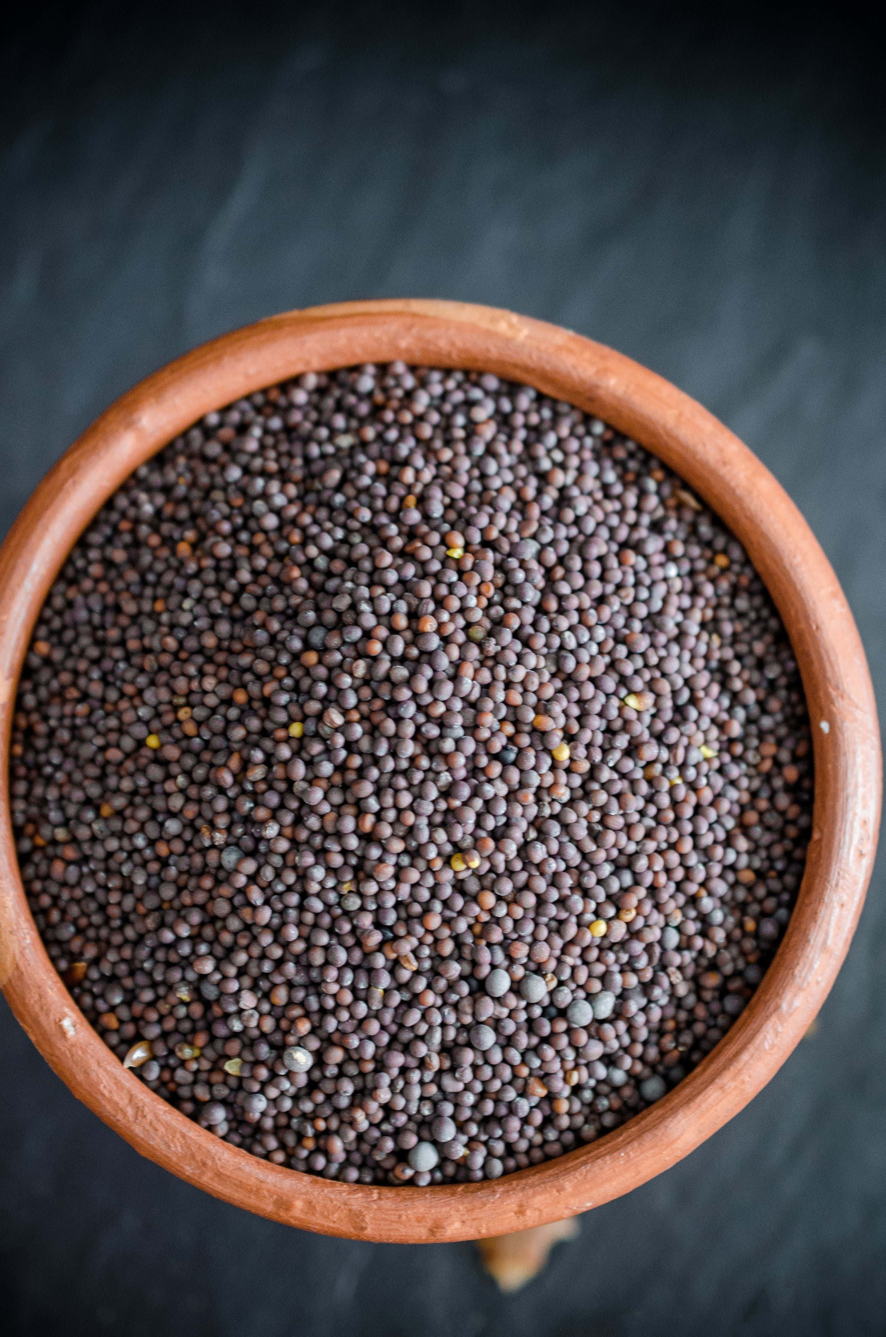 Black Cumin 桌布 壁紙 — 從上方俯瞰一個裝滿深棕色芥末籽的赤陶碗，背景為石板。
