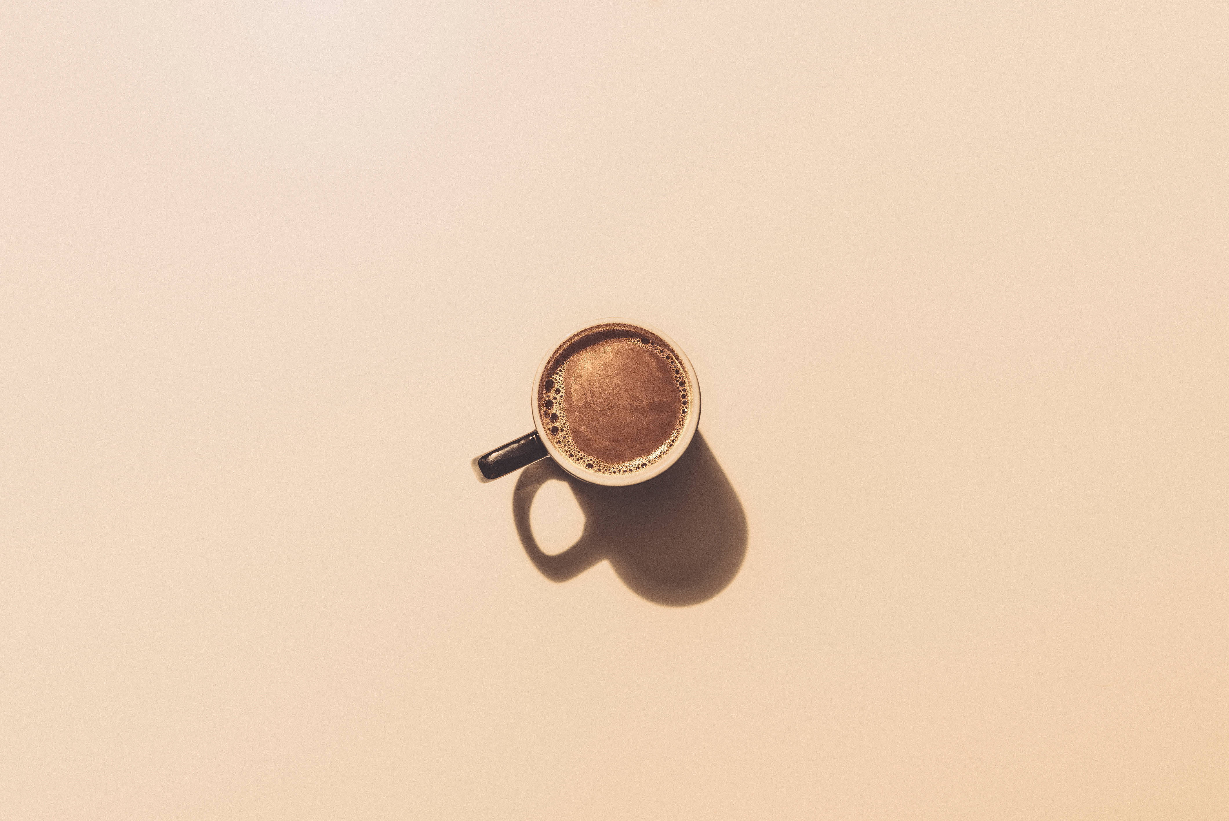 Transient Minimalism 壁紙 — 從上方俯瞰一杯冒煙的咖啡杯，在溫暖的米色表面上投下柔和陰影。