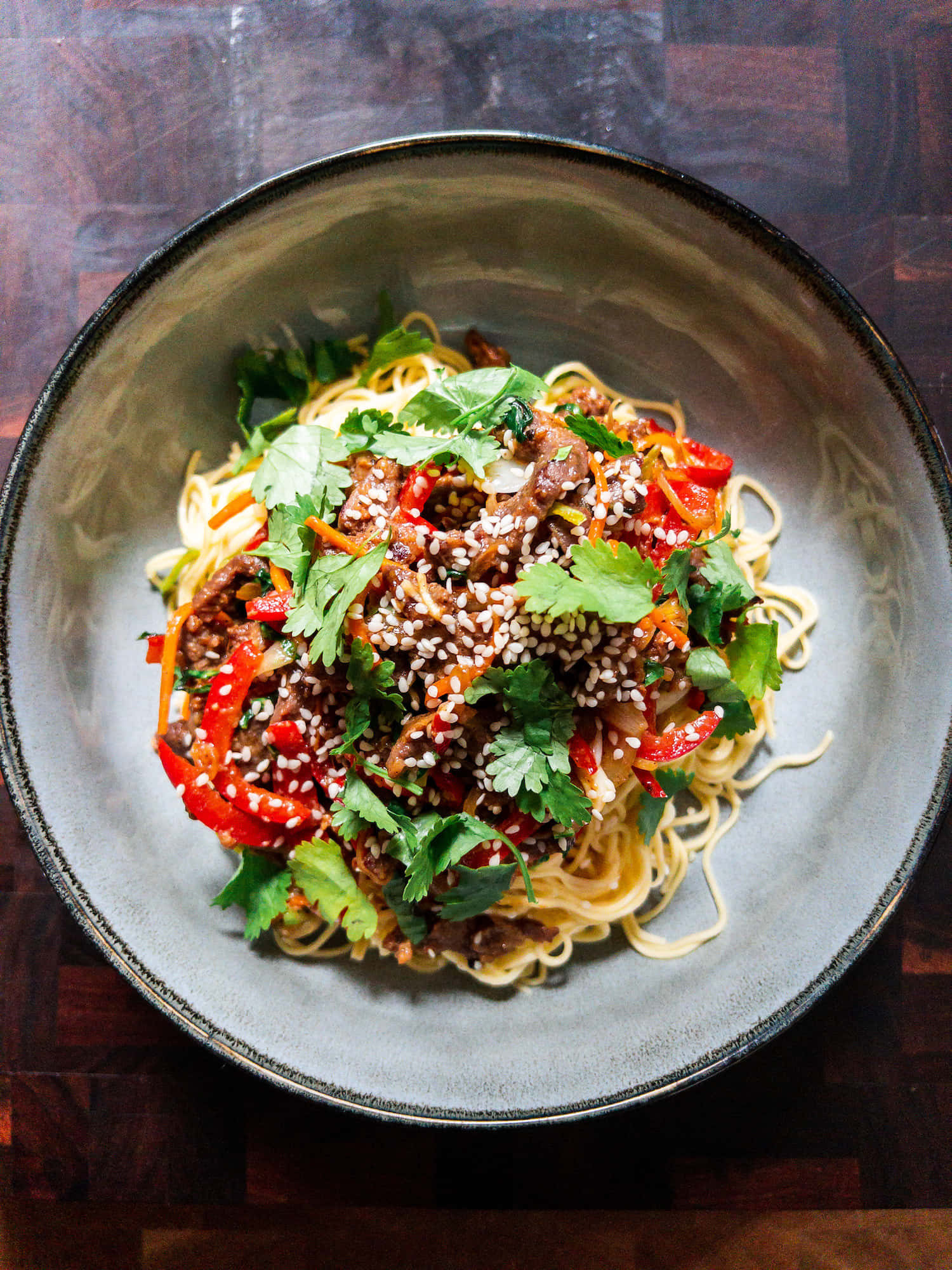 Noodles 桌布 壁紙 — 從上方俯瞰一碗冒煙的炒麵，上面撒有芝麻、芫荽和紅椒。