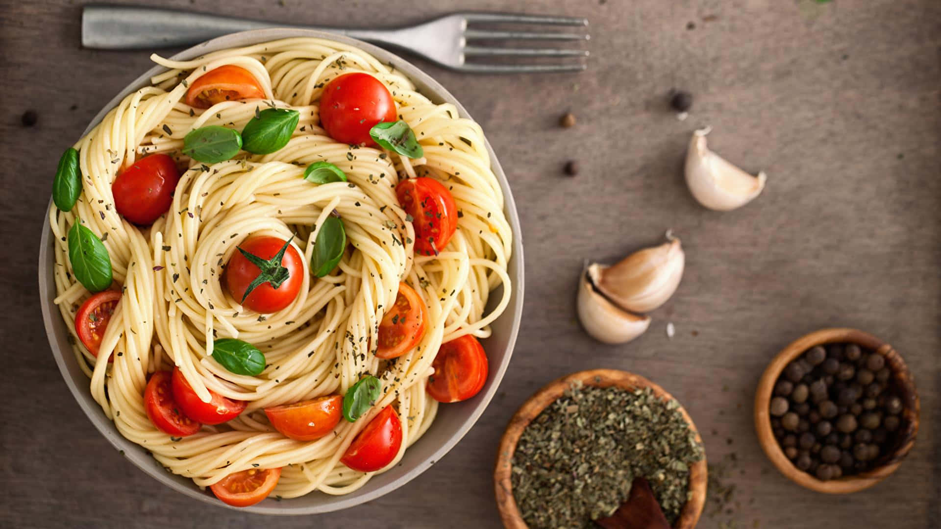 Pasta 桌布 壁紙 — 從上方俯瞰一碗意大利麵，上面鋪滿車厘茄、羅勒和黑胡椒，置於質樸的木質表面上。
