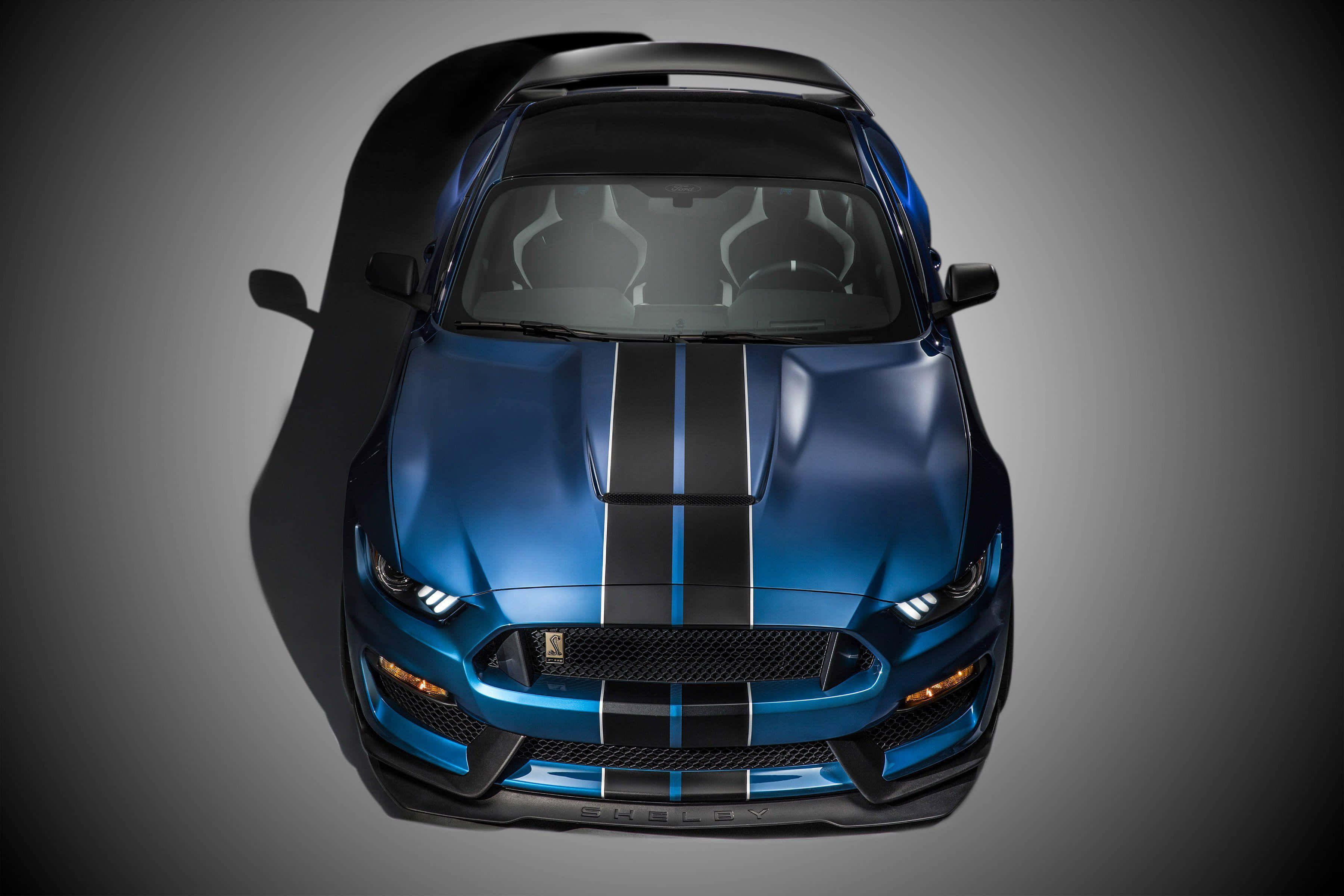 Ford Mustang Shelby Gt350 桌布 壁紙 — 從上方俯瞰一輛帶有黑色賽車條紋的亮藍色跑車，背景為漸變灰色。
