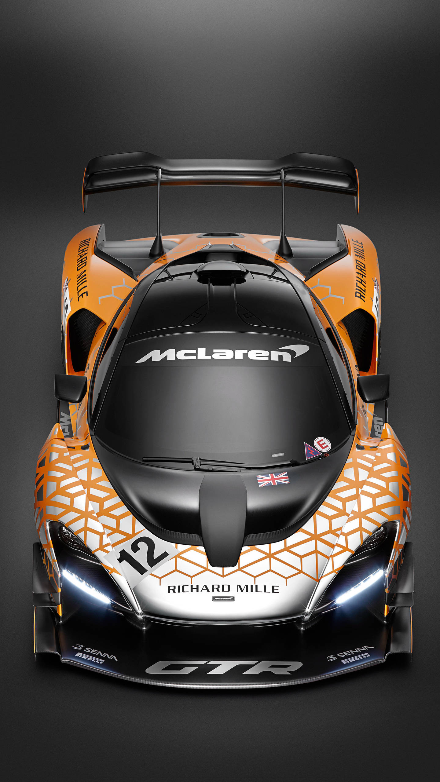 HTC McLaren Senna 壁紙 — 從上方俯瞰一輛時尚的橙色和黑色McLaren Senna GTR賽車，在黑暗的攝影棚背景下帶有發光的車頭燈。