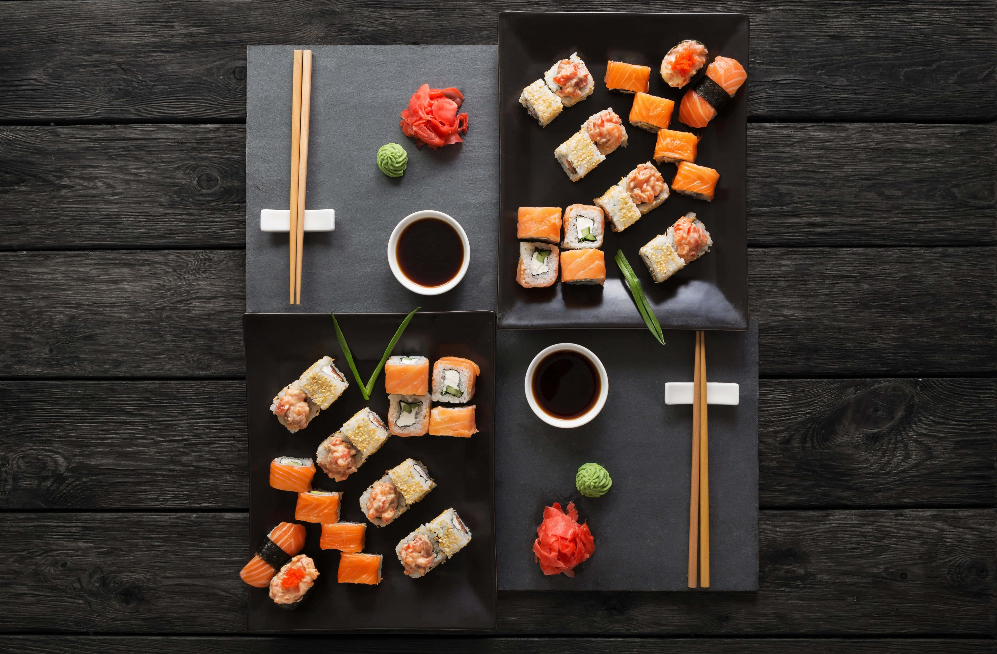 Sushi 桌布 壁紙 — 從上方俯瞰各種壽司卷和刺身放在黑色石板碟上，配以醬油、生薑和芥末，置於深色木桌上。