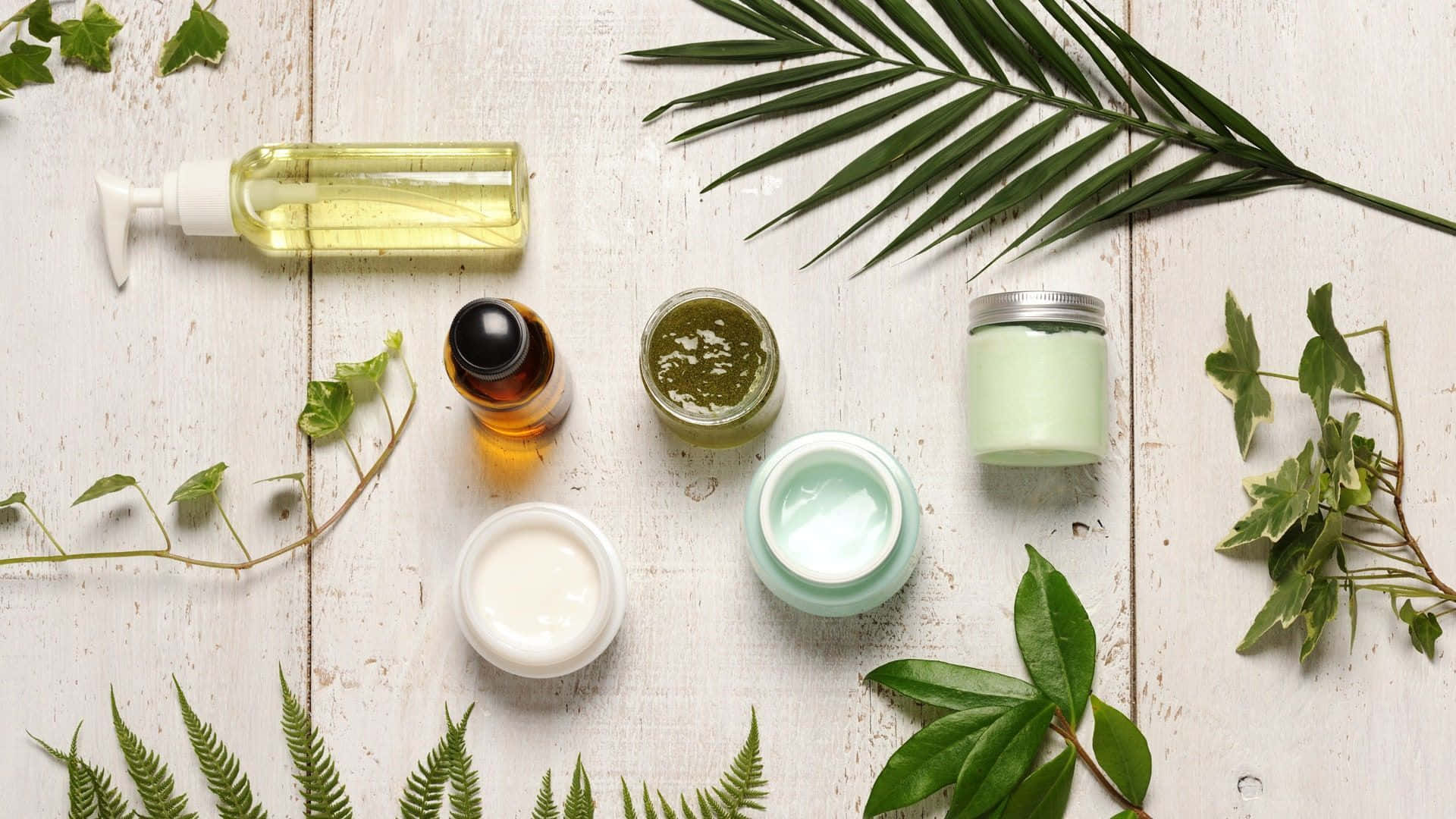 Haircare 桌布 壁紙 — 從上方俯瞰天然護膚產品和新鮮綠色葉子排列在風化的白色木質表面上。