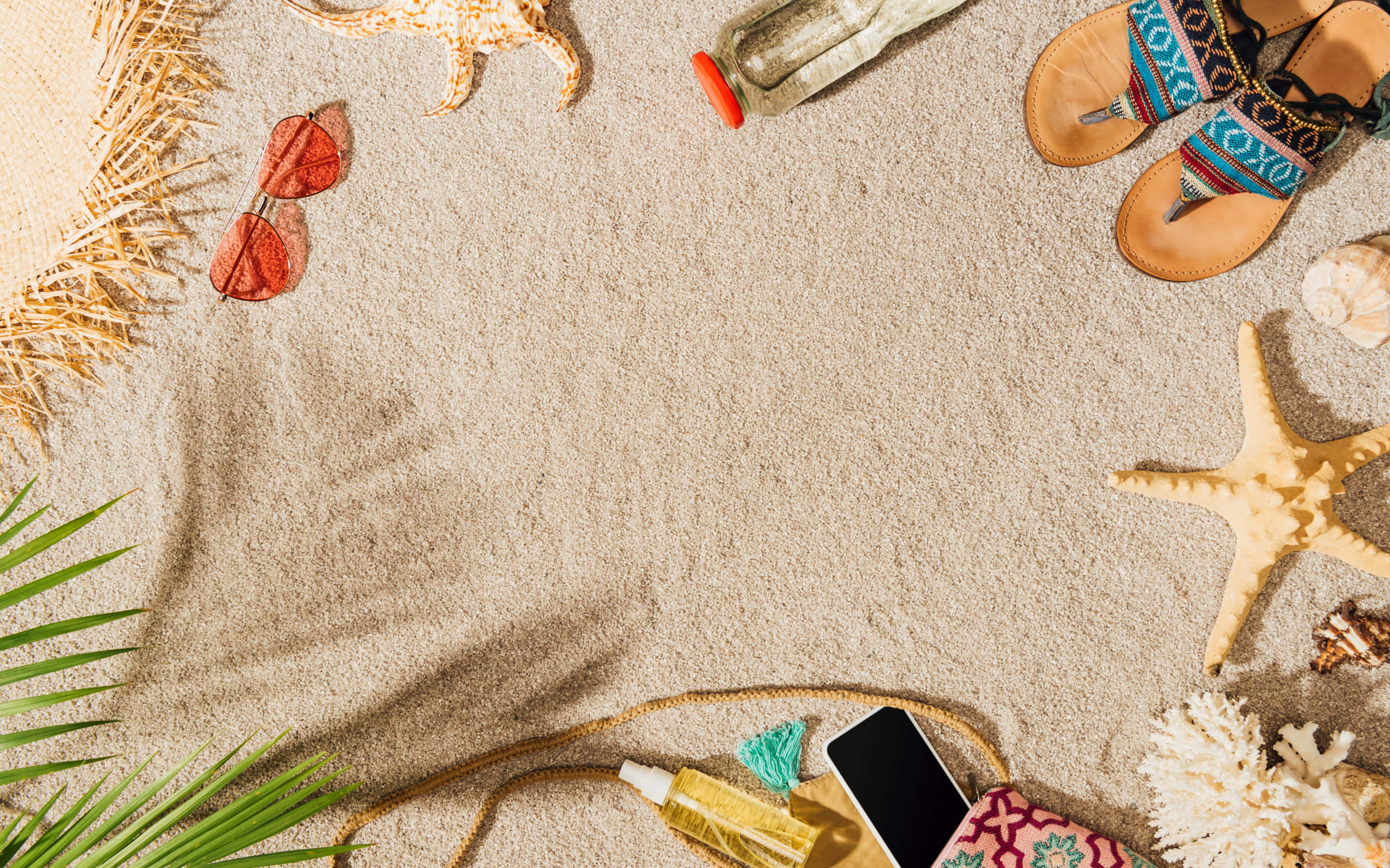 Beach Accessories 桌布 壁紙 — 從上方俯瞰海灘物品，如海星、太陽眼鏡和涼鞋，排列在有紋理的沙子上，並有棕櫚葉。