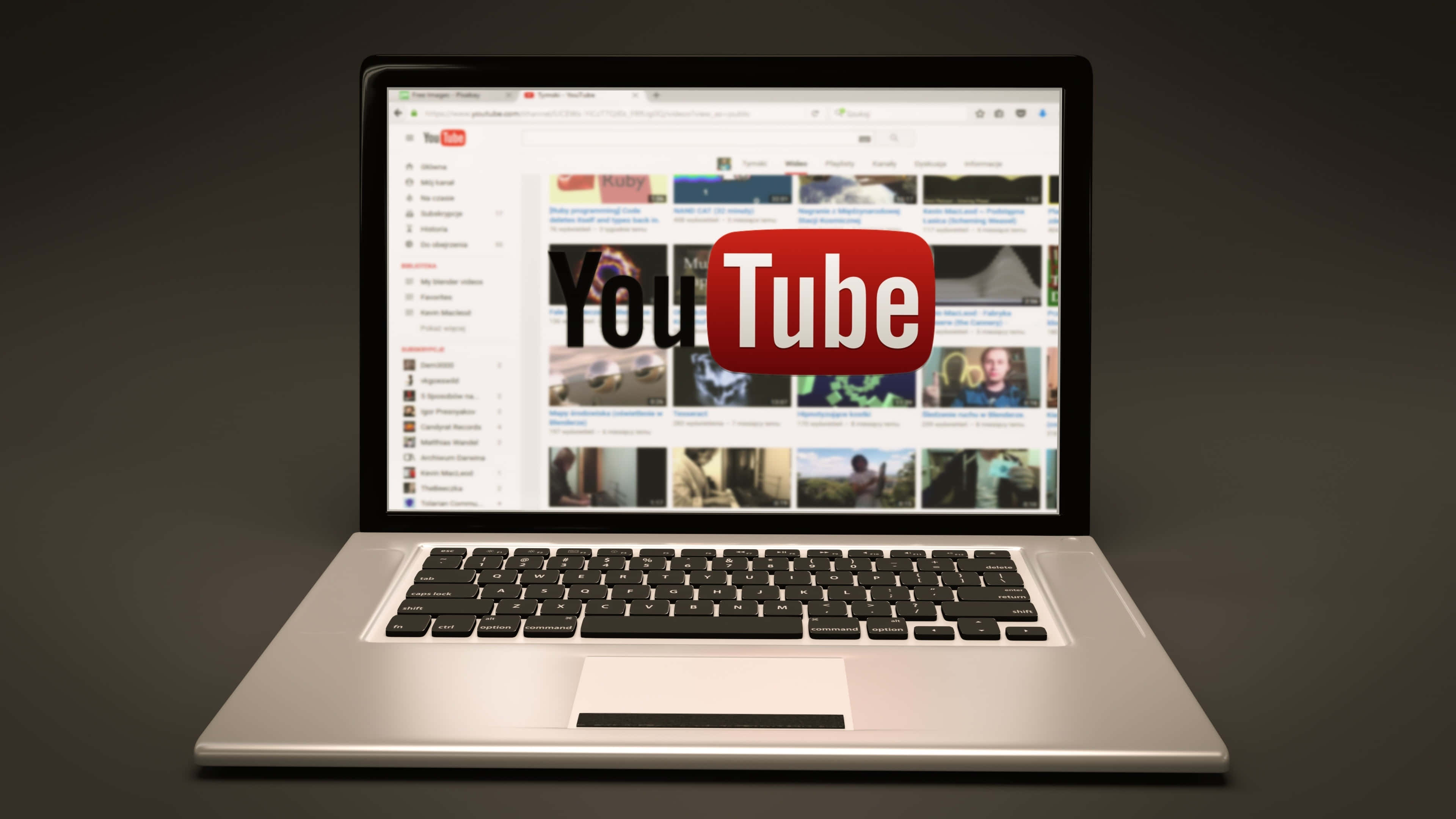 從上方俯瞰的YouTube標誌 壁紙 — 一部時尚的銀色手提電腦顯示YouTube主頁，在深色漸變背景上，影片縮圖中央有一個醒目的紅色標誌。