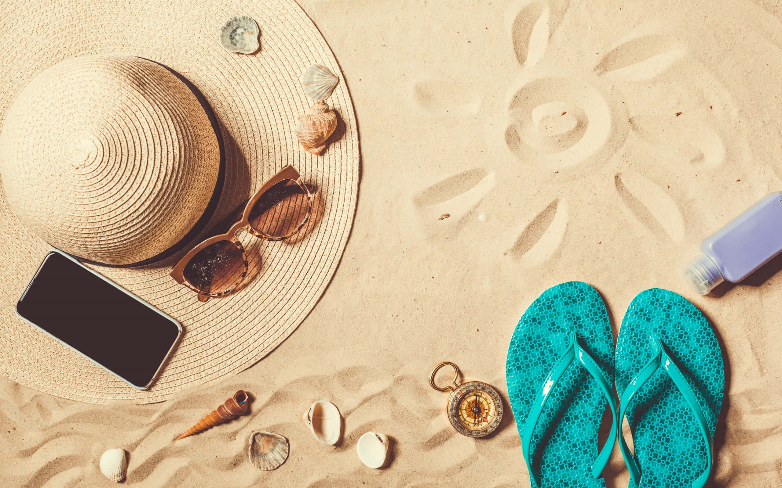 Beach Accessories 桌布 壁紙 — 從上方俯瞰的視角，包括草帽、太陽眼鏡、人字拖和貝殼等沙灘必需品，排列在金色沙灘上。