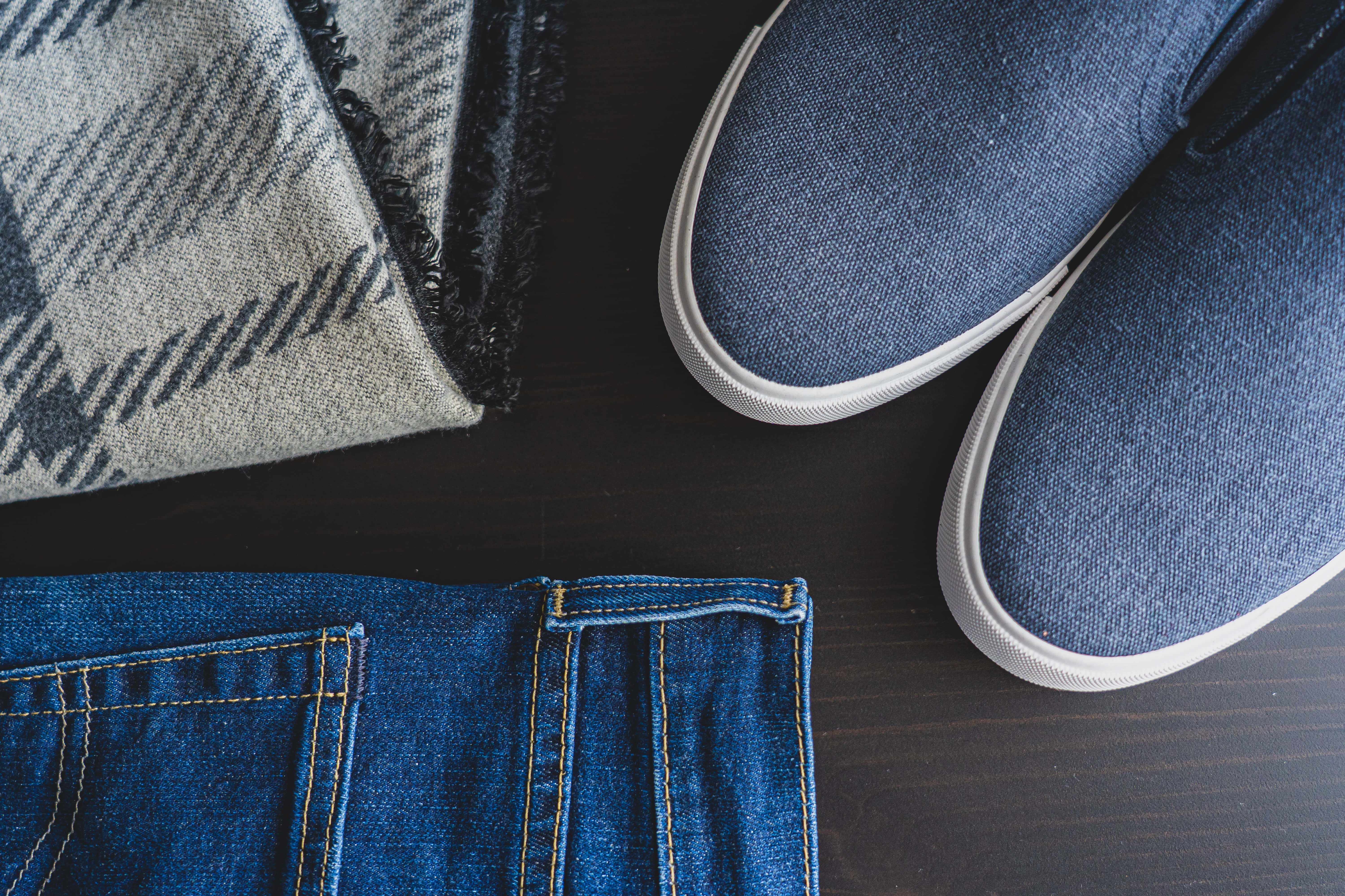 Navy Blue Shoes 桌布 壁紙 — 從上方俯瞰藍色牛仔褲口袋、藍色 slip-on 運動鞋和灰色格仔圍巾擺放在深色木質表面上的景象。
