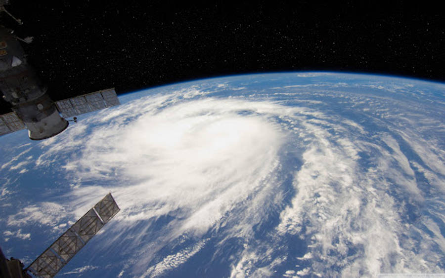 從外太空拍攝的颶風 壁紙 — 從太空站的角度看，一場巨大的颶風在繁星點點的黑色天空中盤旋在地球的藍色海洋上。