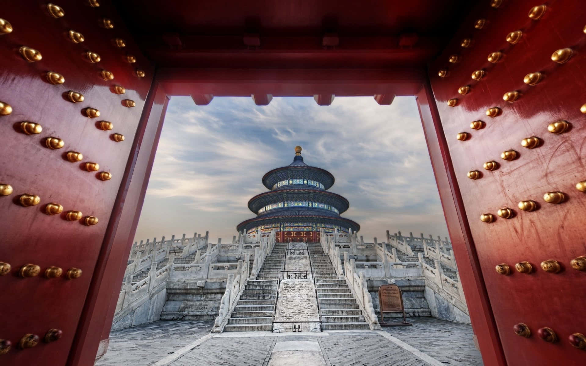紅門框住了多層雄偉寺廟，石階在陰天天空下。