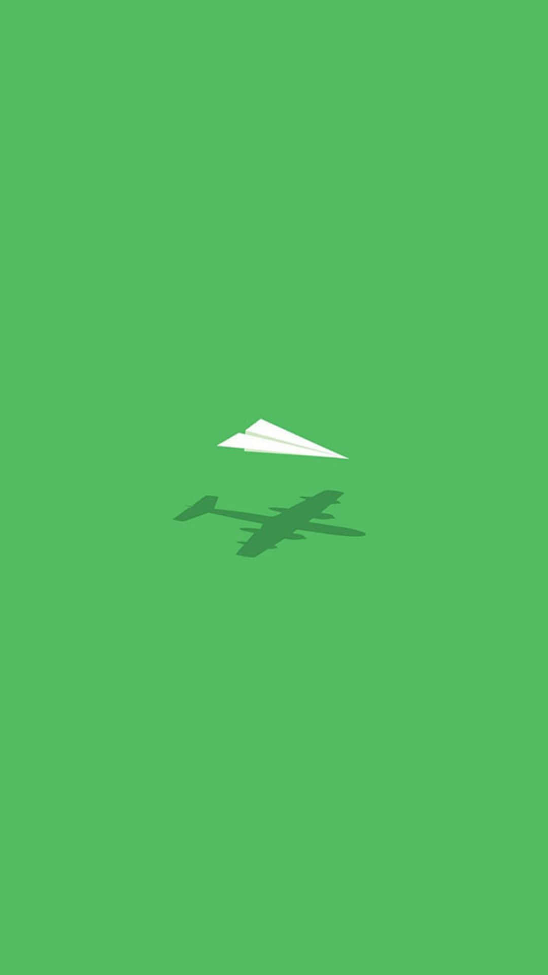 從天空俯瞰小飛機的美麗風景 壁紙 — 一個簡約的綠色背景，上面有一架白色紙飛機在較深色的綠色飛機剪影上方翱翔。