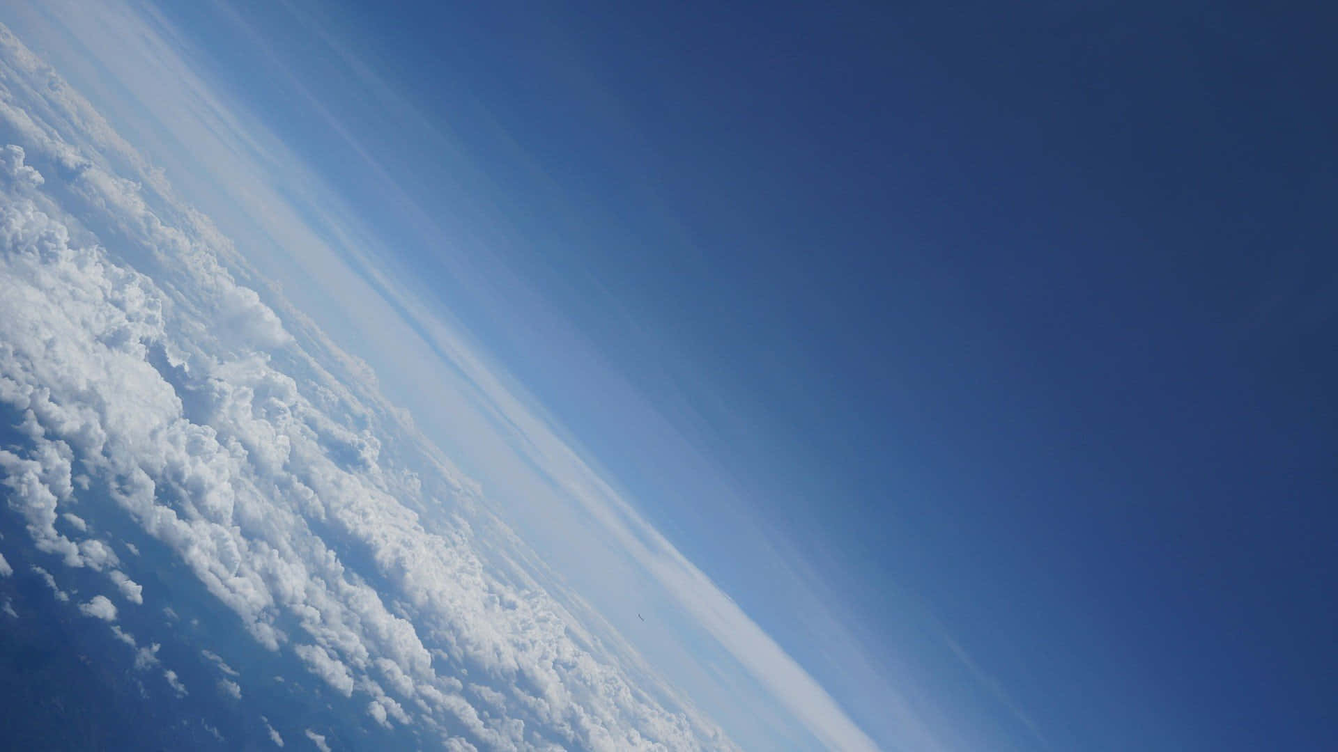 Atmosphere 桌布 壁紙 — 從太空俯瞰地球彎曲地平線的壯麗景色，下方是蓬鬆的白雲，上方是深藍色的天空。