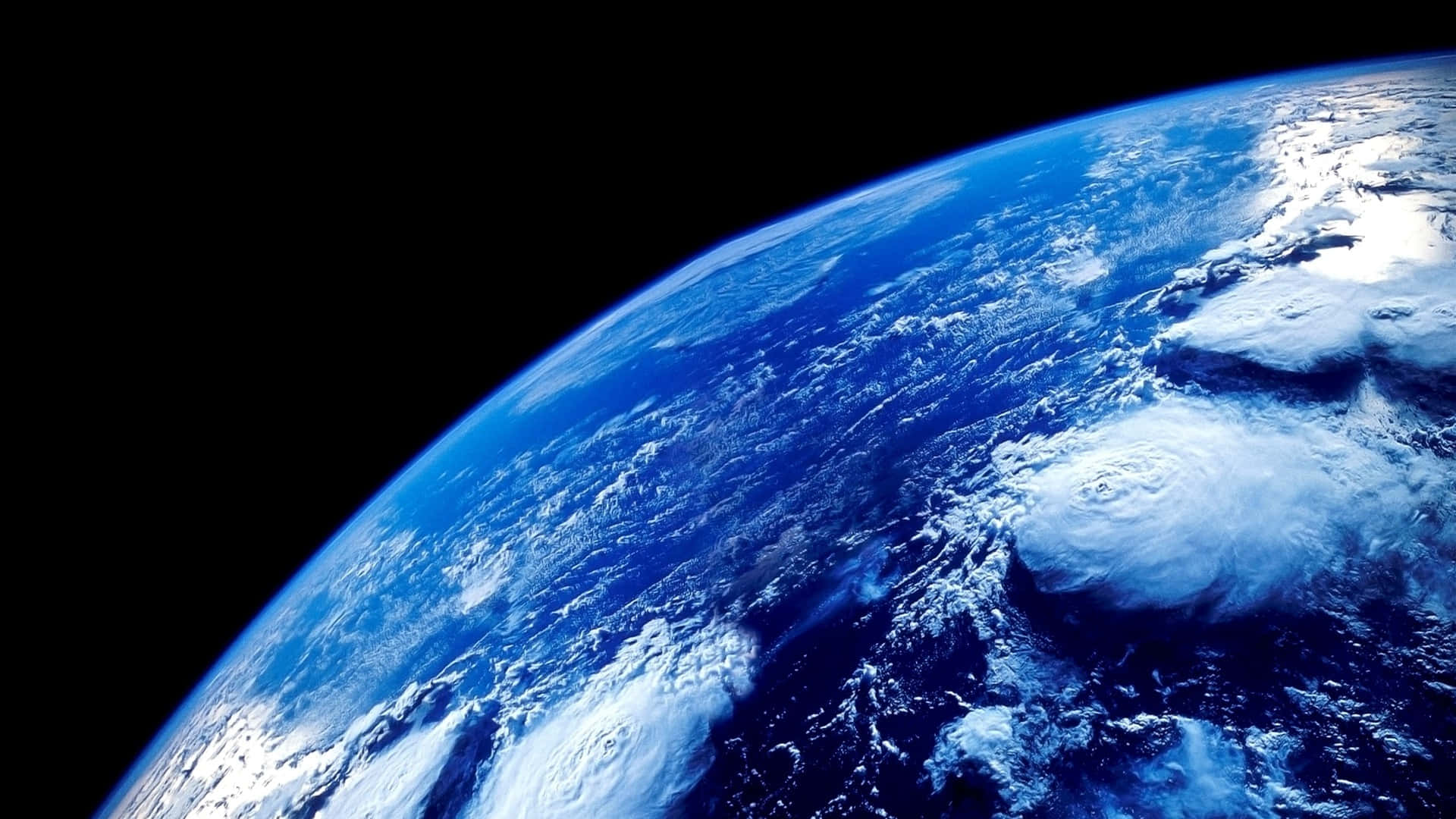 Blue Planet 桌布 壁紙 — 從太空俯瞰地球的壯麗景色，展示深藍色海洋和積雪覆蓋的陸地上方旋轉的白色雲層，背景是漆黑的虛空。