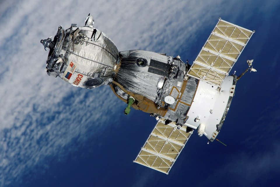 從太空衛星拍攝宇宙 壁紙 — 一艘詳細的俄羅斯太空船帶有太陽能電池板，在藍色海洋和白色雲層的背景下繞地球運行。