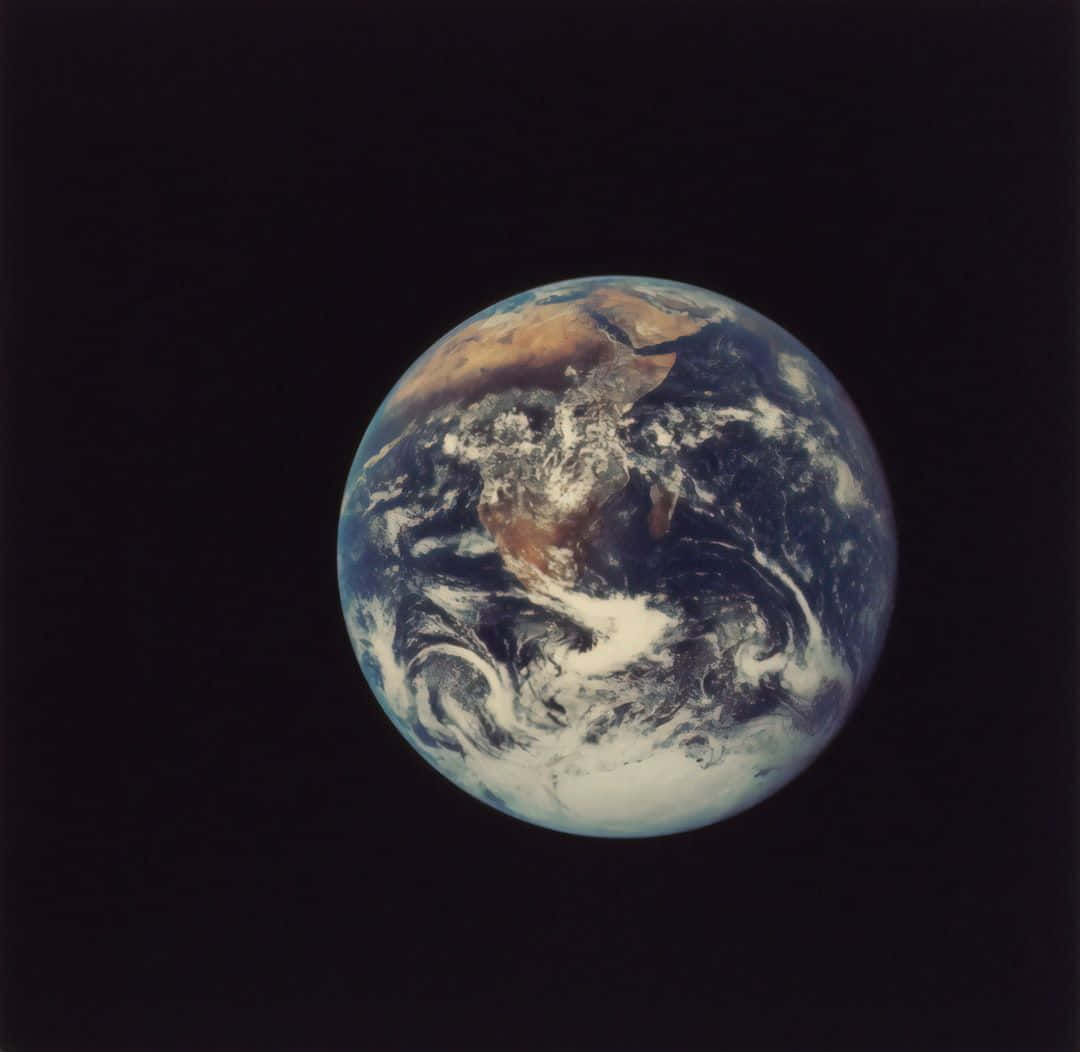 3d Earth 桌布 壁紙 — 從太空觀看地球，顯示藍色海洋、棕色大陸和旋轉的白色雲朵，背景是黑色虛空。