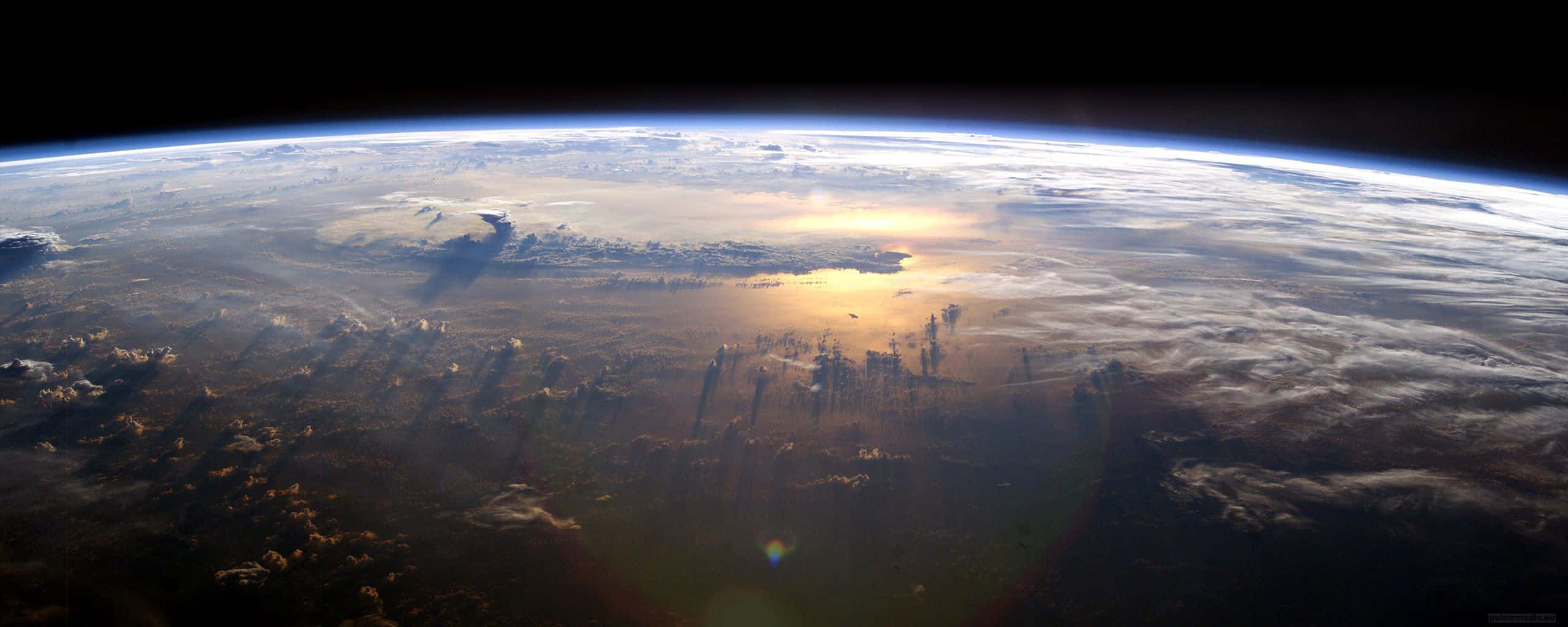 Earth Science 桌布 壁紙 — 從太空觀看地球在日出時，金色光芒照亮雲層和海洋，襯托著黑色虛空。