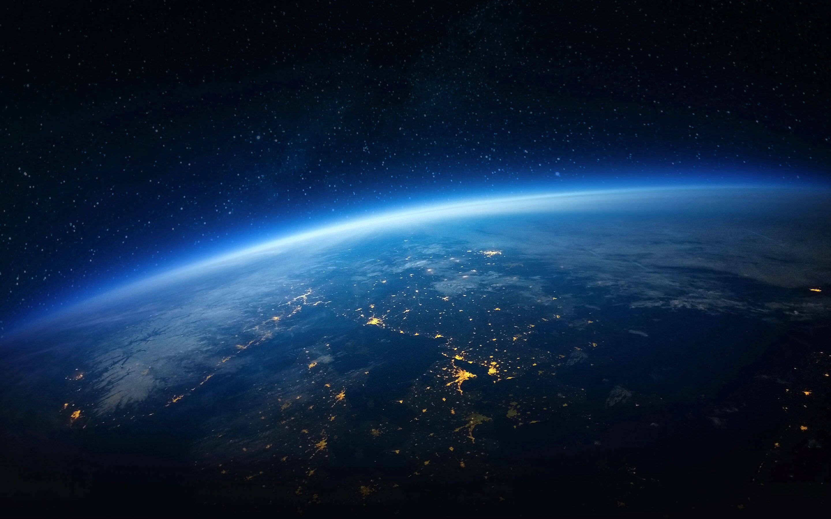 地球 桌布 壁紙 — 從太空觀看夜晚的地球，城市燈光在繁星點點的黑色天空和藍色大氣輝光中閃耀。