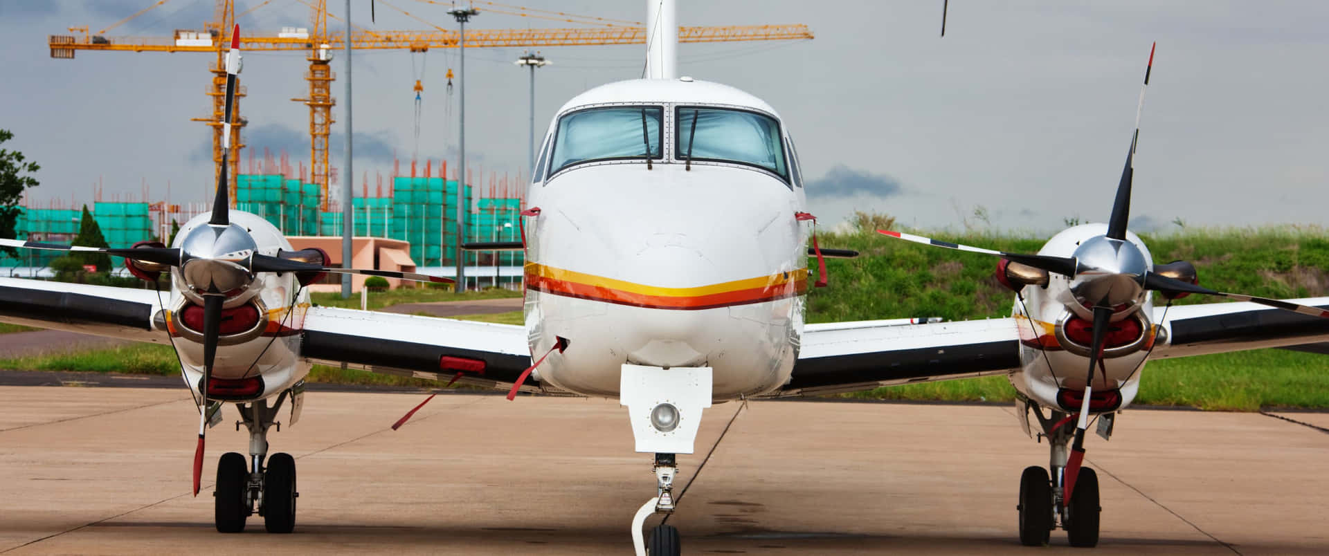 白色雙引擎螺旋槳飛機停泊在建築工地附近的停機坪上。