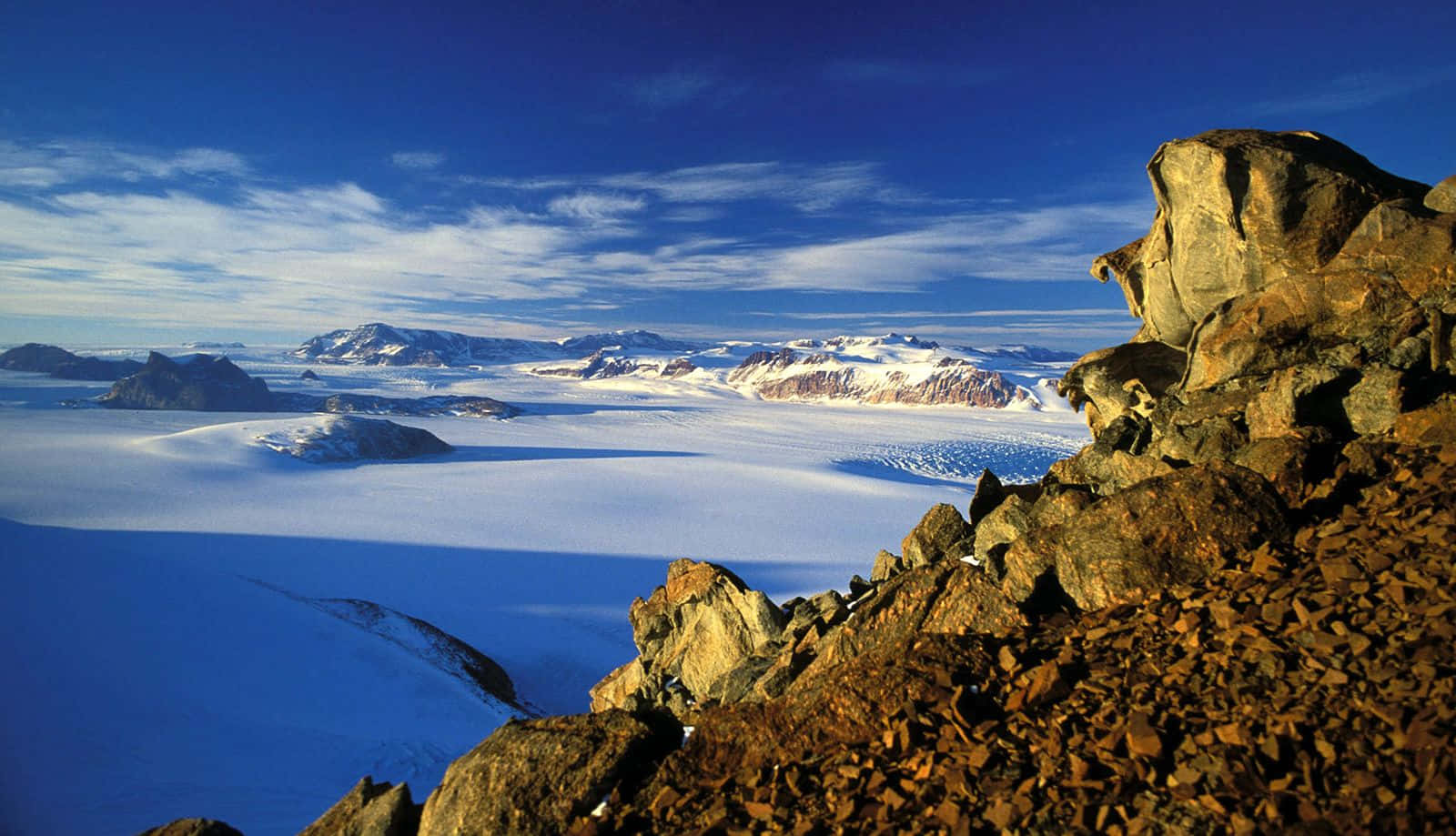 Antarctica 桌布 壁紙 — 從岩石露頭俯瞰廣闊冰河的壯麗景色，天空湛藍，雲彩輕柔。
