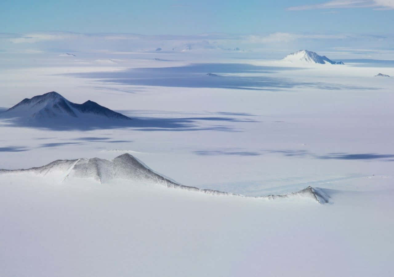 Antarctica 桌布 壁紙 — 從廣闊冰原上升起的積雪火山峰頂的鳥瞰圖，背景是淡藍色的天空。