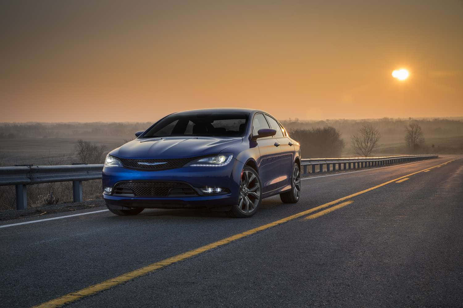 從強悍有力到時尚精緻，Chrysler 車款貼合每種生活型態 壁紙 — 一架時尚的藍色轎車在金色夕陽下沿著鄉村高速公路行駛，溫暖的陽光灑滿整個場景。