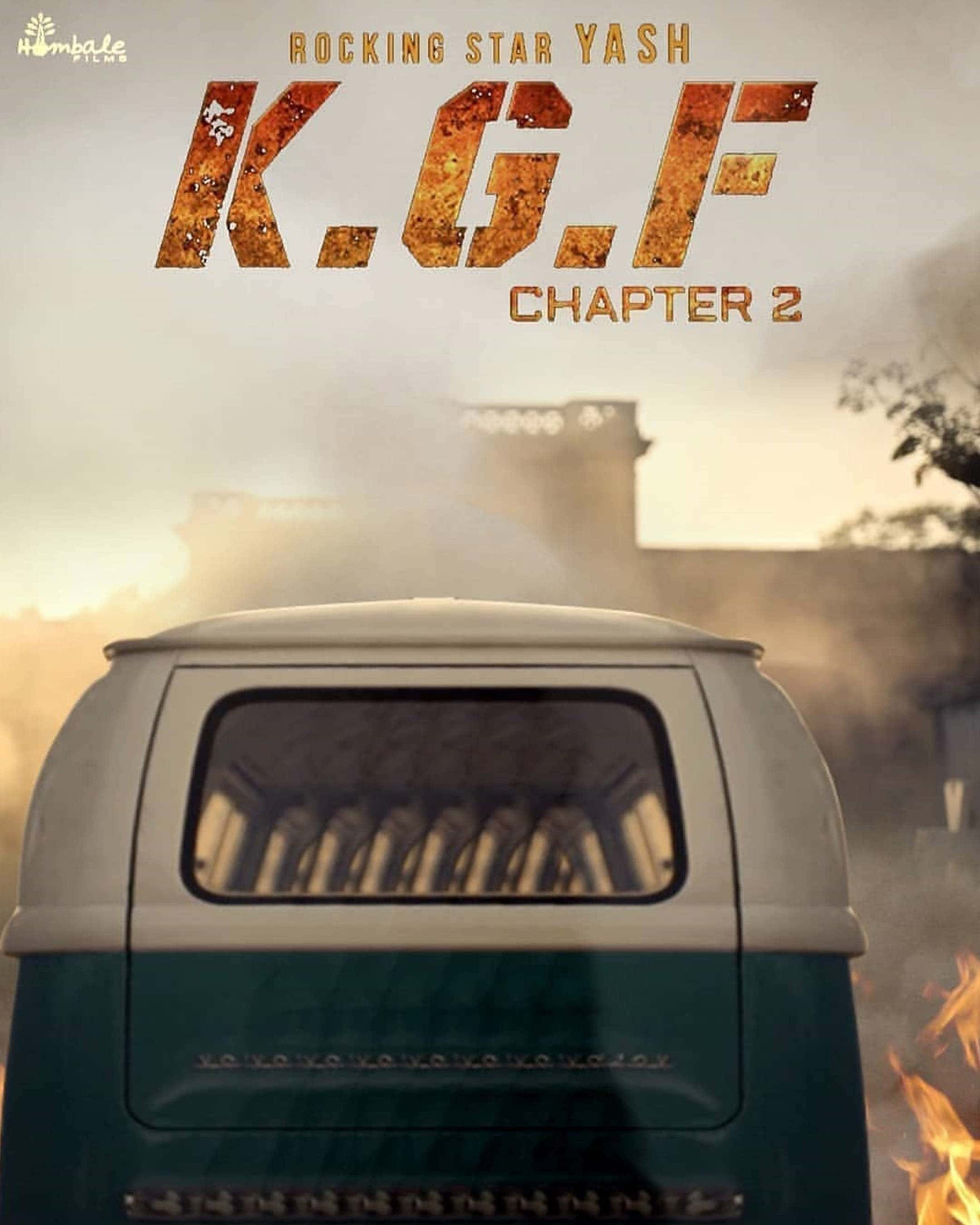 Kgf Chapter 2 桌布 壁紙 — 從後方看到的復古青綠色和白色貨車，右側有火焰，遠處建築物後方有朦朧的日落天空。