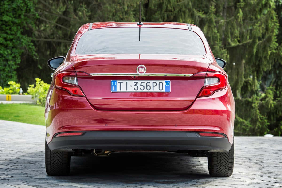 Fiat Tipo 桌布 壁紙 — 從後方觀看一輛亮紅色快意轎車停泊在石頭車道上，背景是茂密的綠樹。