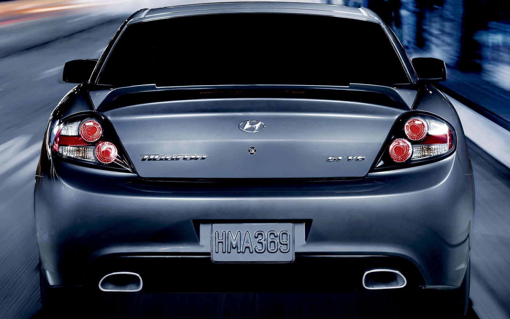 Hyundai Tiburon 桌布 壁紙 — 從後方觀看一輛時尚深藍色現代Tiburon GT V6在夜間模糊高速公路上疾馳。