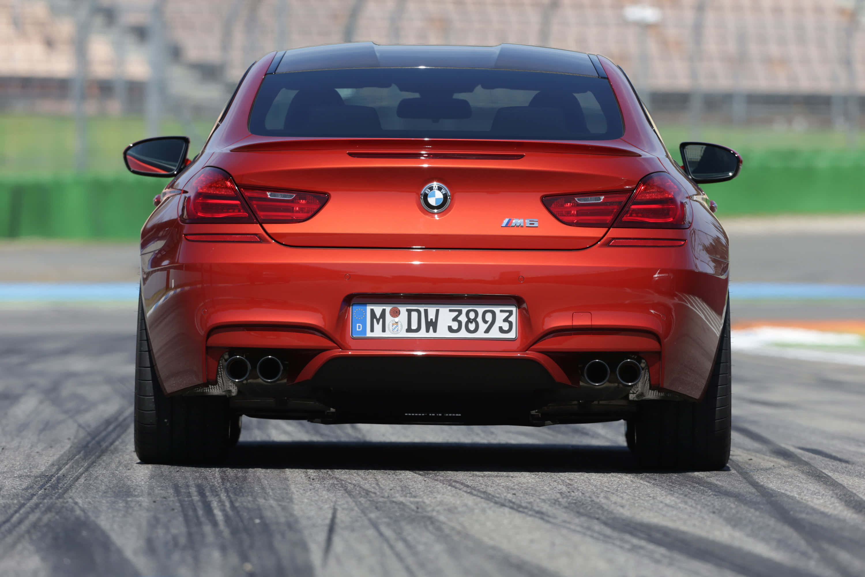 Bmw M6 桌布 壁紙 — 從後方觀看一輛鮮紅色BMW M6雙門跑車在賽道上，遠方有模糊的看台。