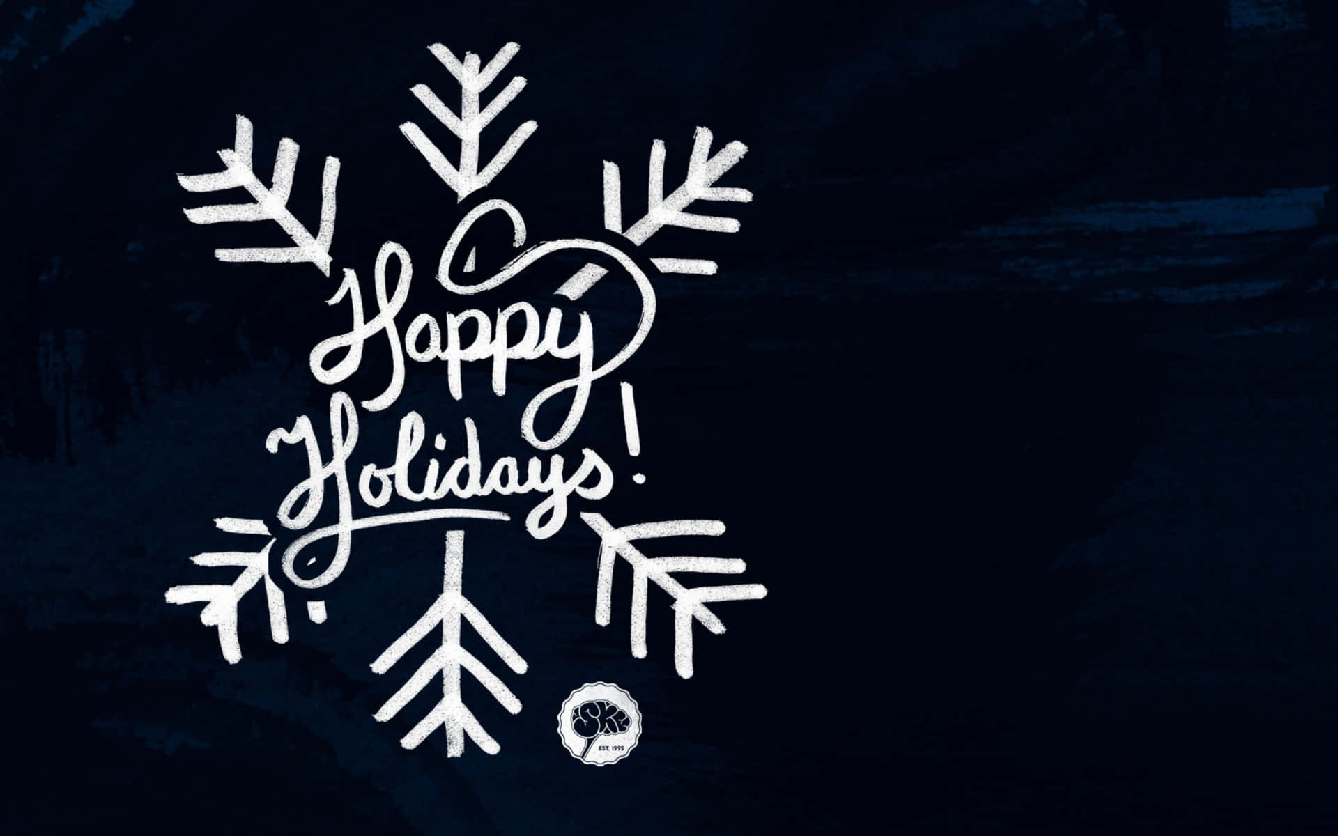 從您的桌面享受節日歡樂 壁紙 — 白色草書 'Happy Holidays!' 文字嵌在雪花設計中，背景為有紋理的深藍色。