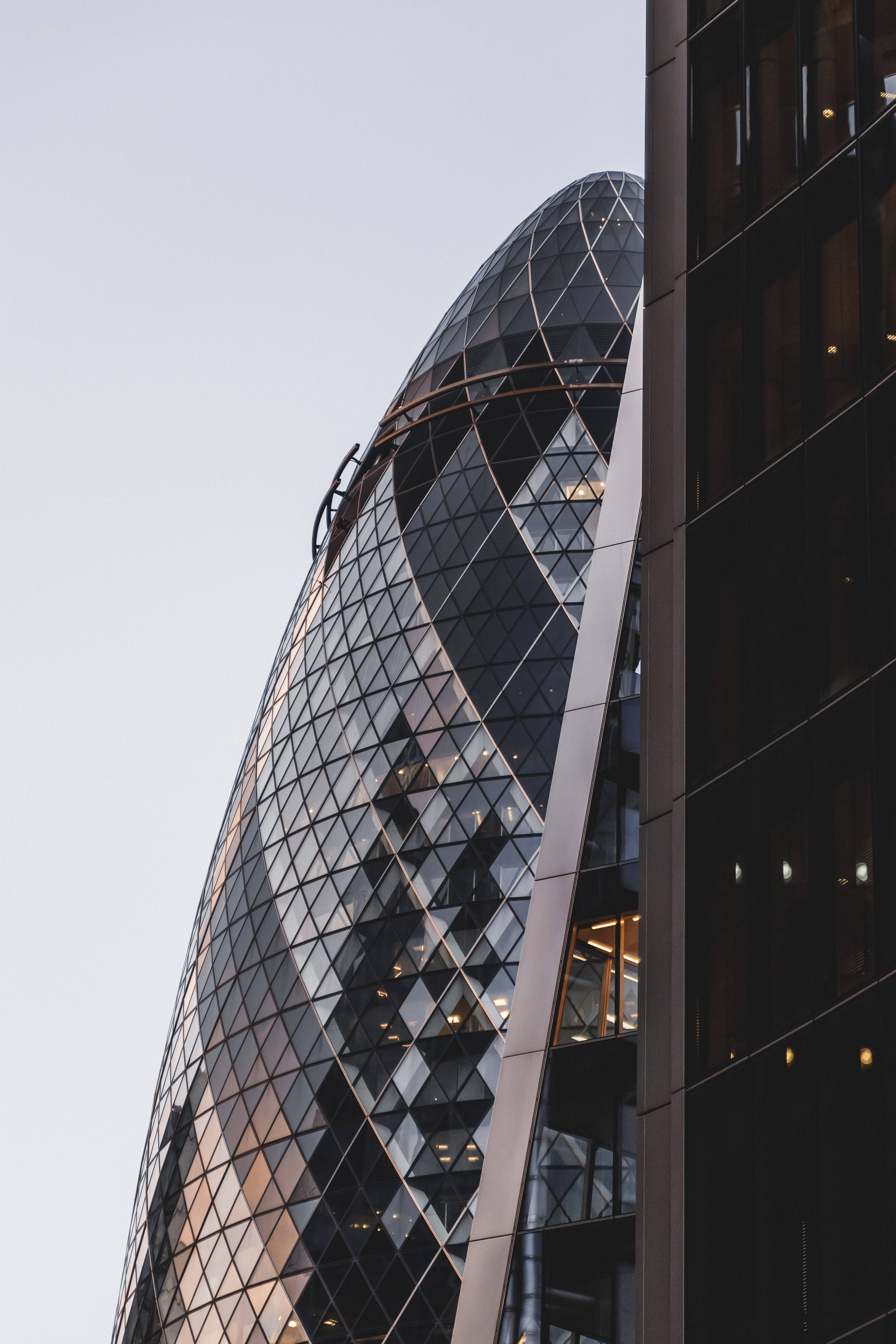 從旁觀角度拍攝的The Gherkin 壁紙 — 標誌性小黃瓜大廈玻璃幕牆的特寫，映照著城市燈光，背景是淡色的天空。