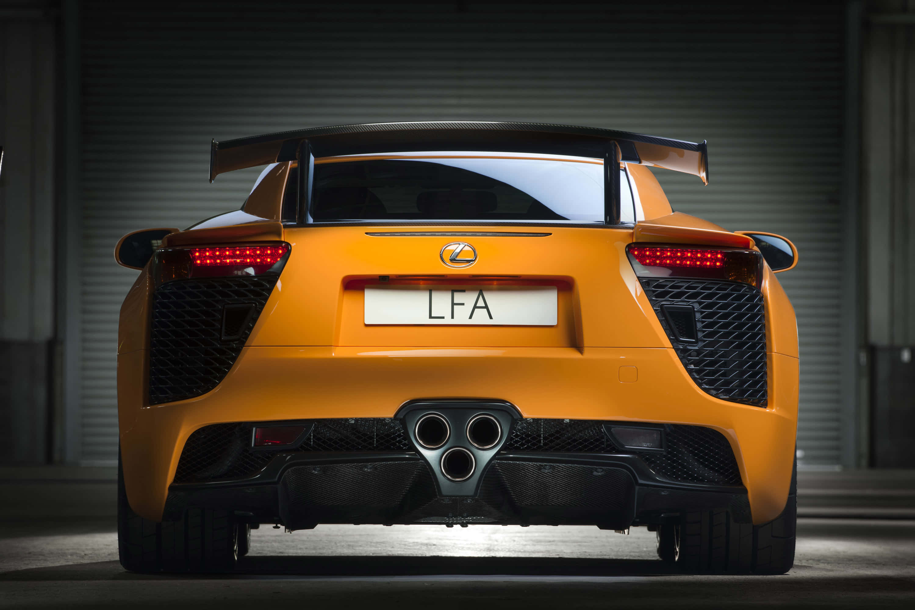 Lexus Lfa 桌布 壁紙 — 從昏暗車庫後方觀看鮮橙色Lexus LFA超級跑車，帶有發光紅色尾燈和碳纖維擾流板。