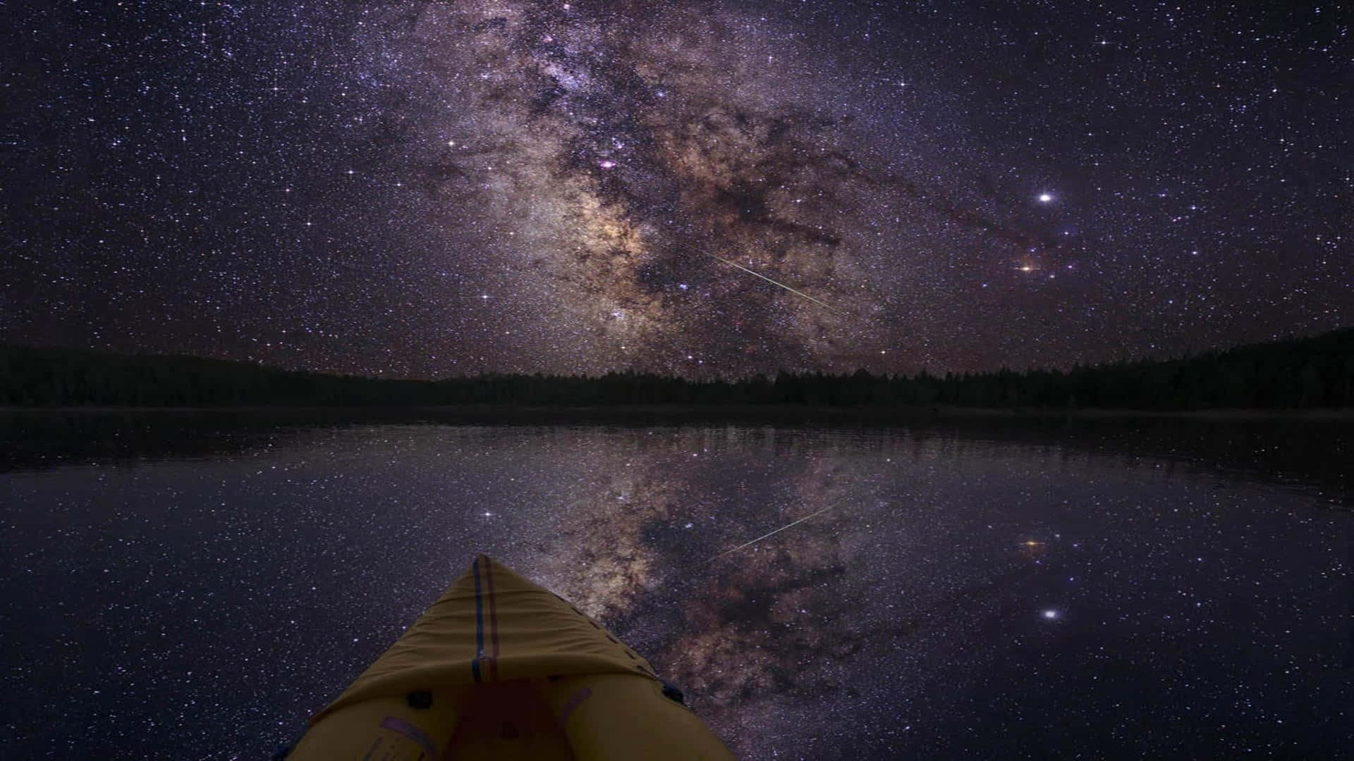 繁星夜空下湖面上的黃色皮划艇，帶有銀河倒影