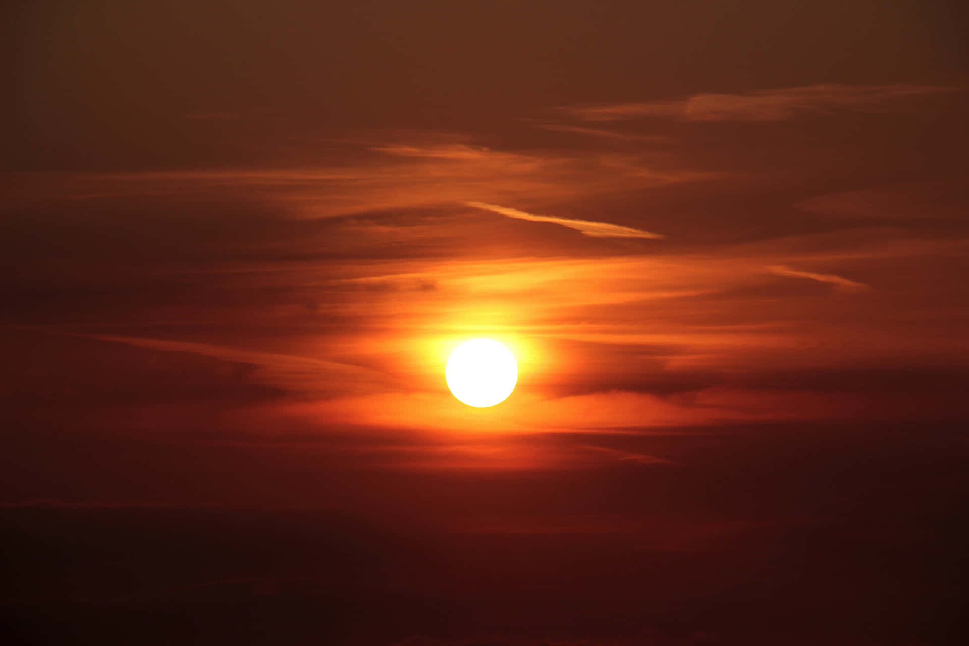 明亮的太陽在戲劇性的天空中落在橙色雲彩後面。