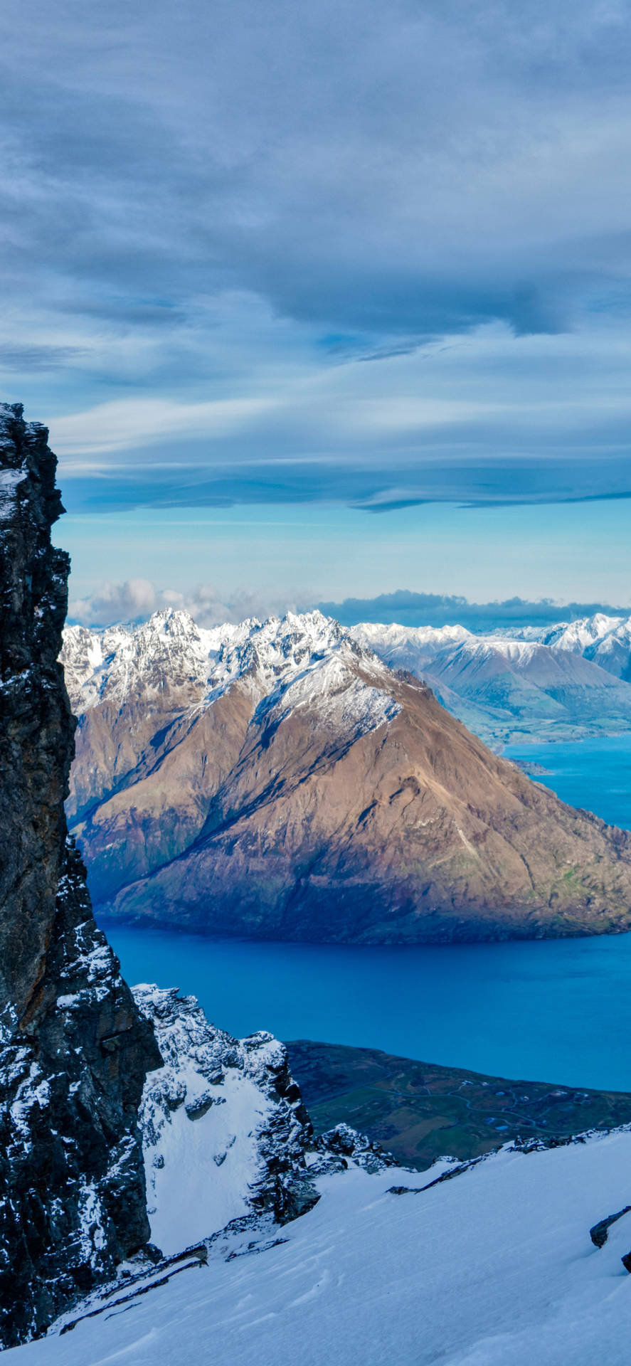 白雪覆蓋的山崖，俯瞰碧綠湖泊，遠方山峰在藍天下。 — 海景 壁紙