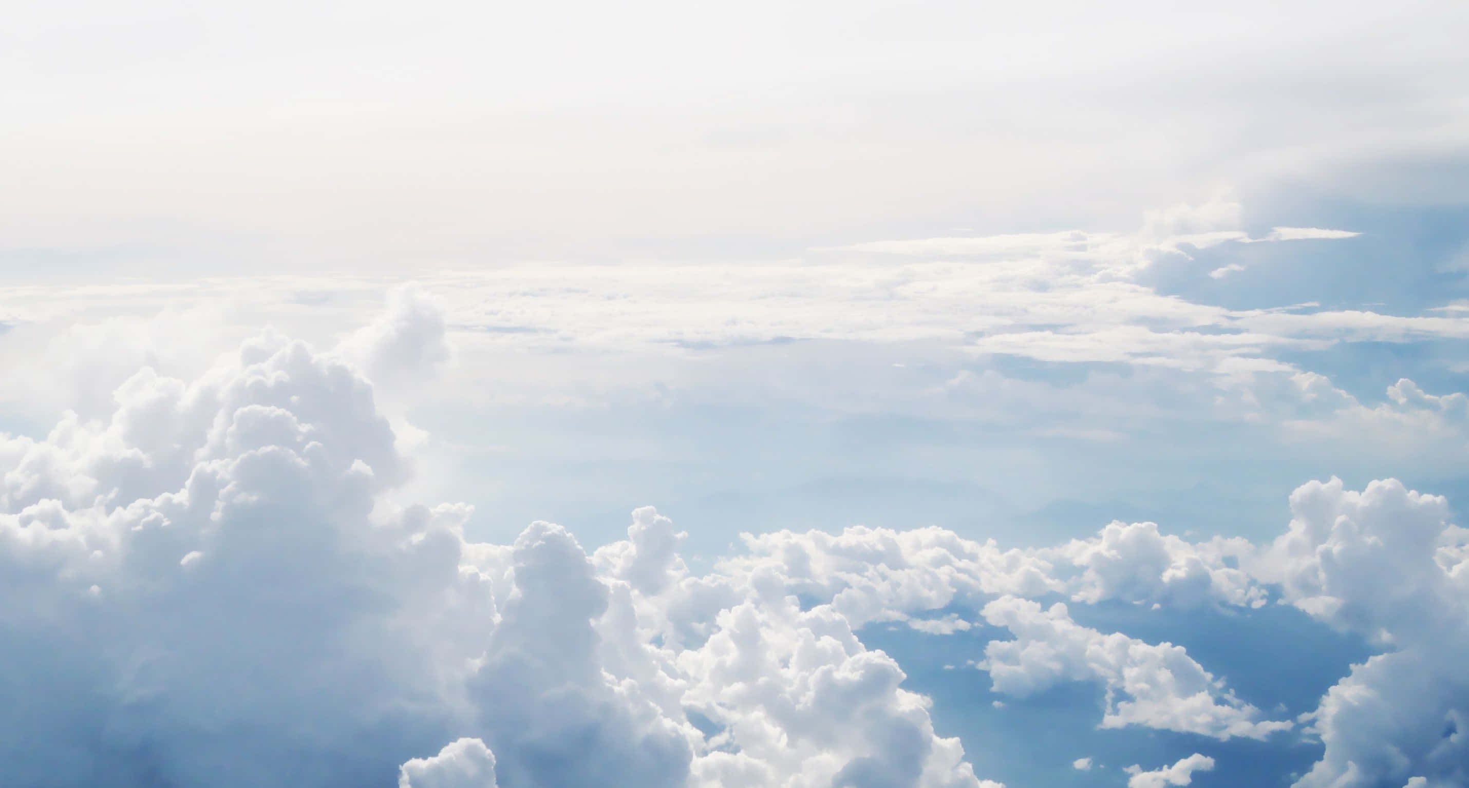 Cloud Aesthetic 桌布 壁紙 — 從空中俯瞰，柔軟的白雲在淡藍色的天空中延伸，下方是遙遠的山脈。