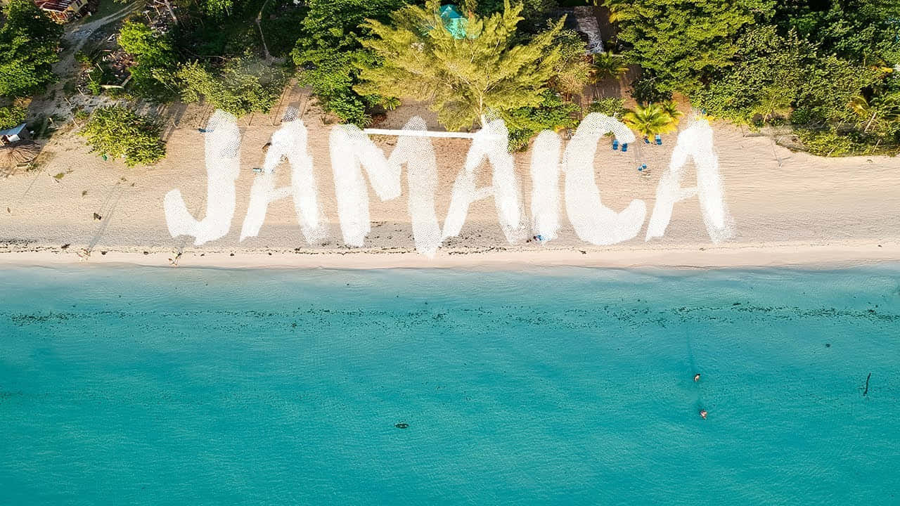 Jamaican Island 桌布 壁紙 — 從空中俯瞰熱帶海灘上以白沙拼寫的「JAMAICA」，周圍有碧綠的海水和茂密的綠樹。