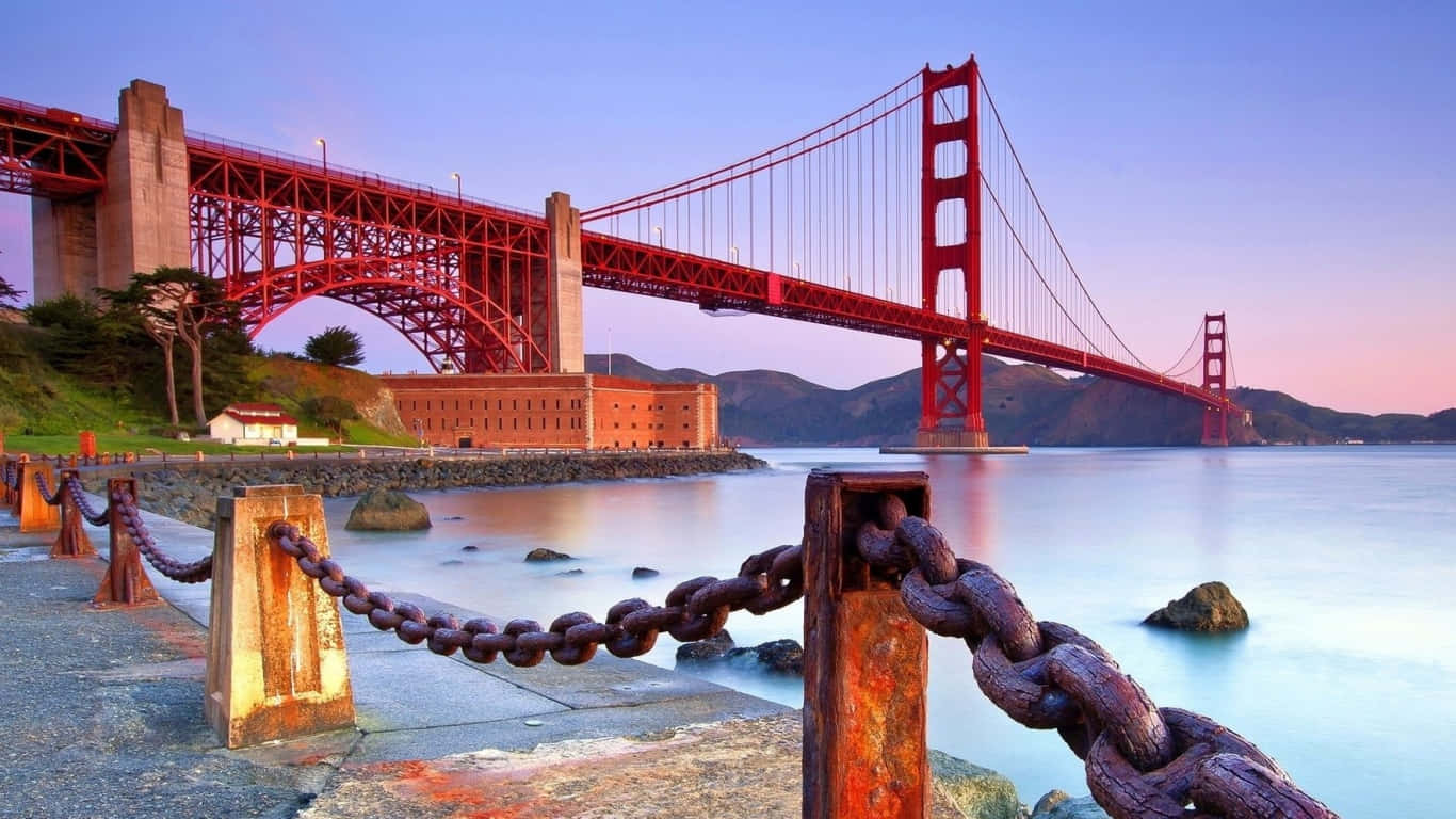 日落時分的金門大橋，前景有生鏽的鐵鏈圍欄
