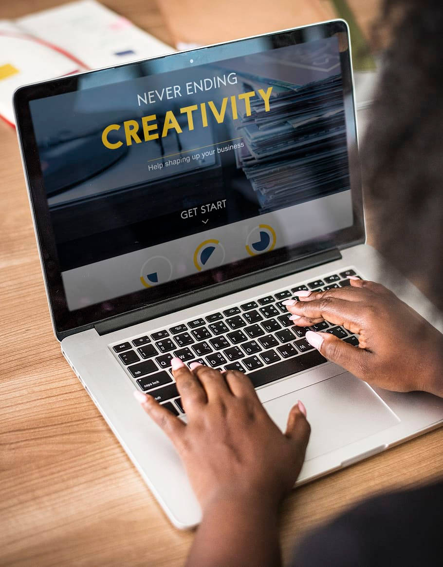  壁紙 — 從肩膀後方觀看一個人在筆記型電腦上打字，顯示 'Never Ending Creativity' 商業網站。
