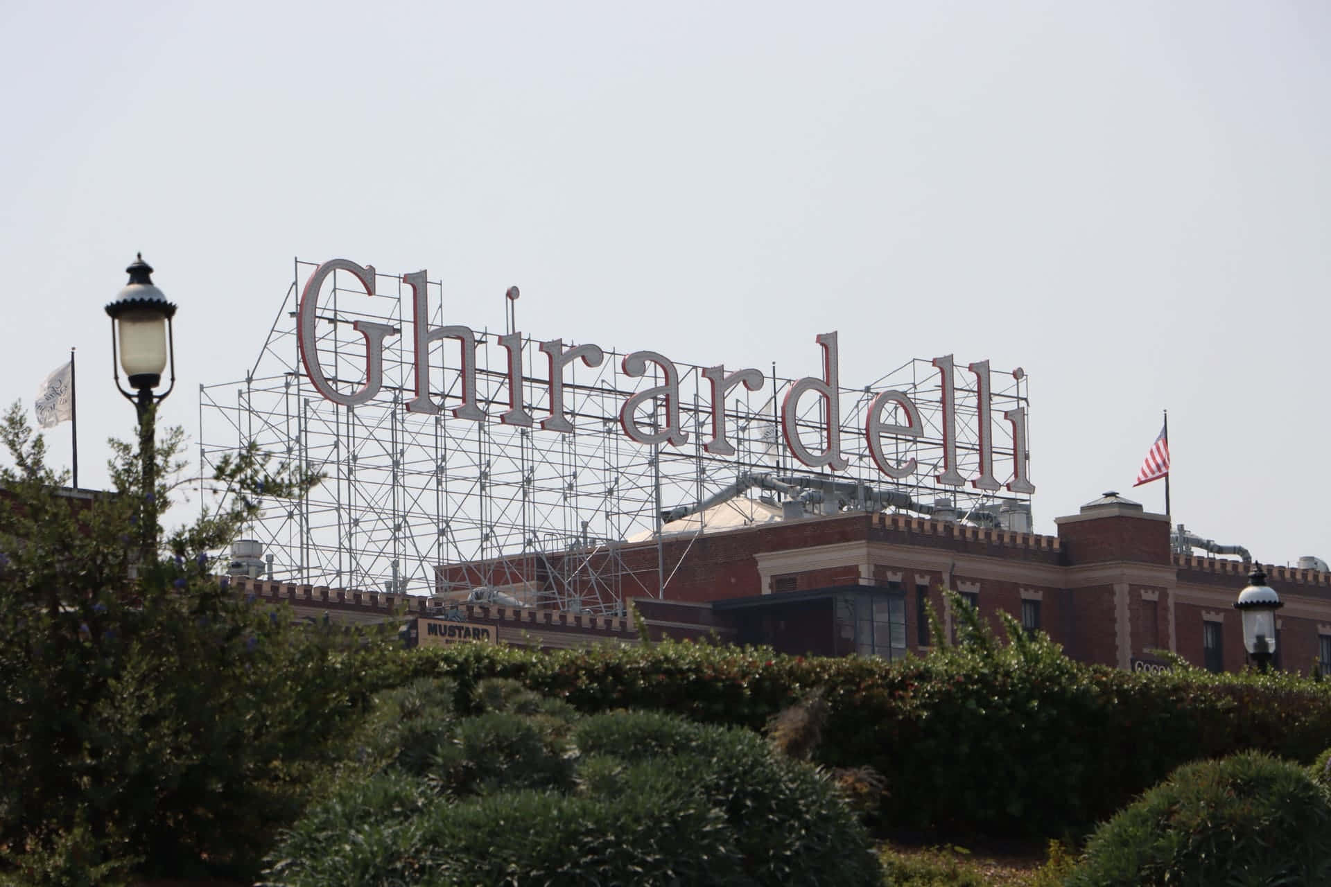 Ghirardelli 標誌正在磚建築上施工，有綠色樹籬和路燈。