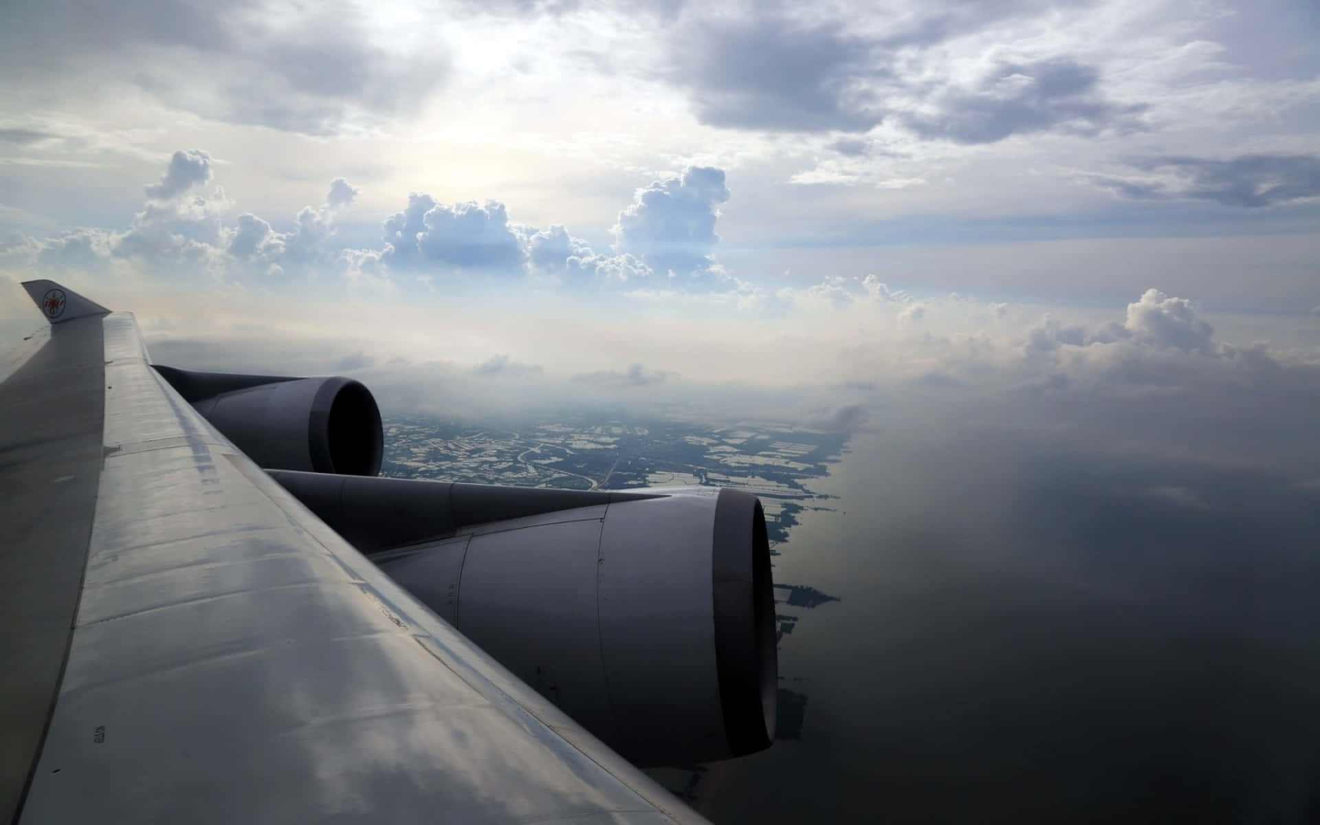 Aviation 桌布 壁紙 — 從飛機窗戶俯瞰，在戲劇性的多雲天空下，海岸景觀上方的機翼引擎。